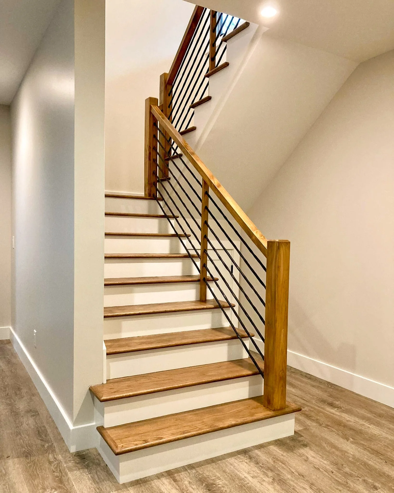 Wooden staircase with black metal railings leading upward, carpeted steps, beige walls, and wood flooring.