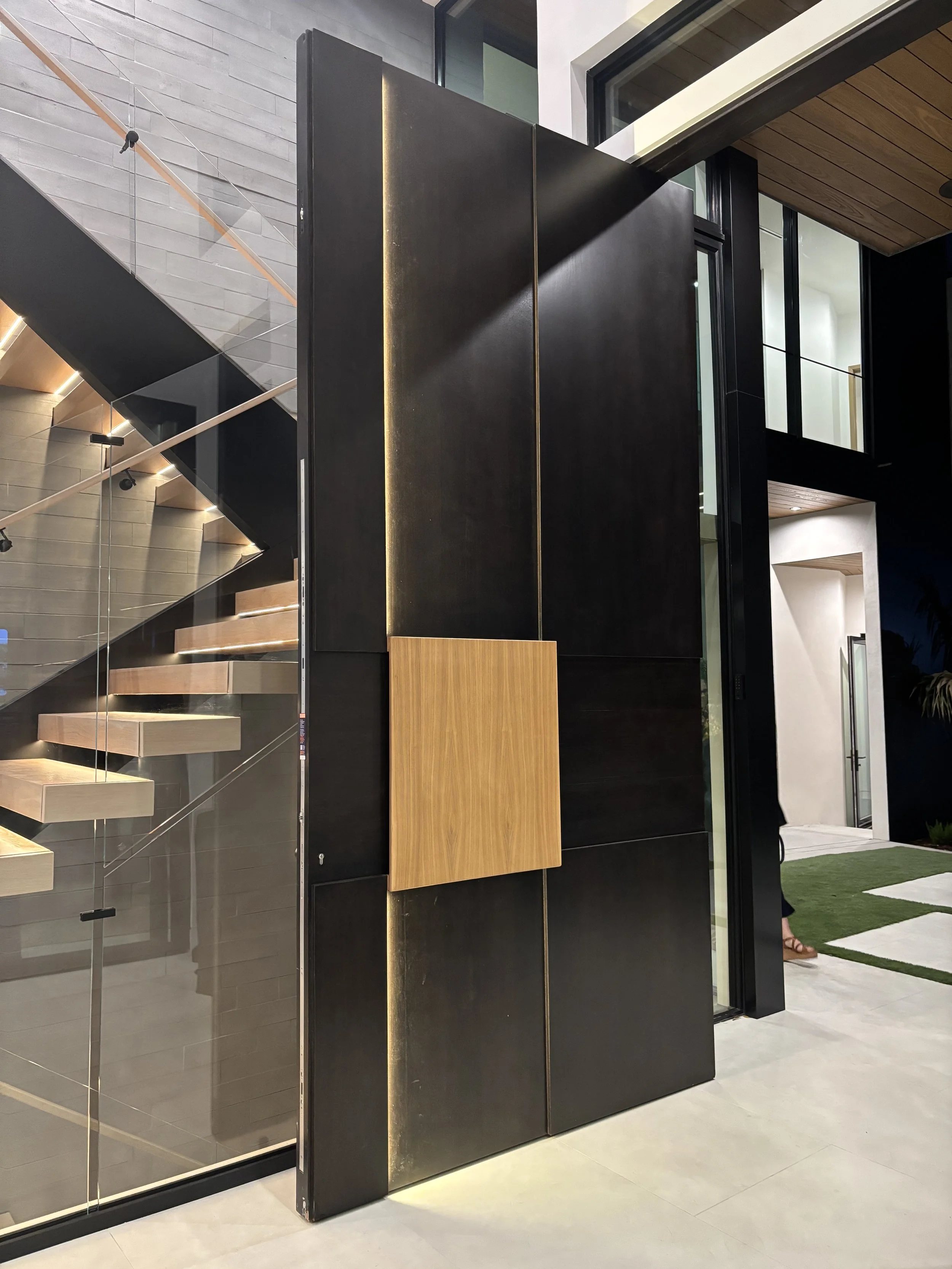 Modern interior with a staircase and glass wall, featuring black walls, wood accents, and a partially visible person in the background.