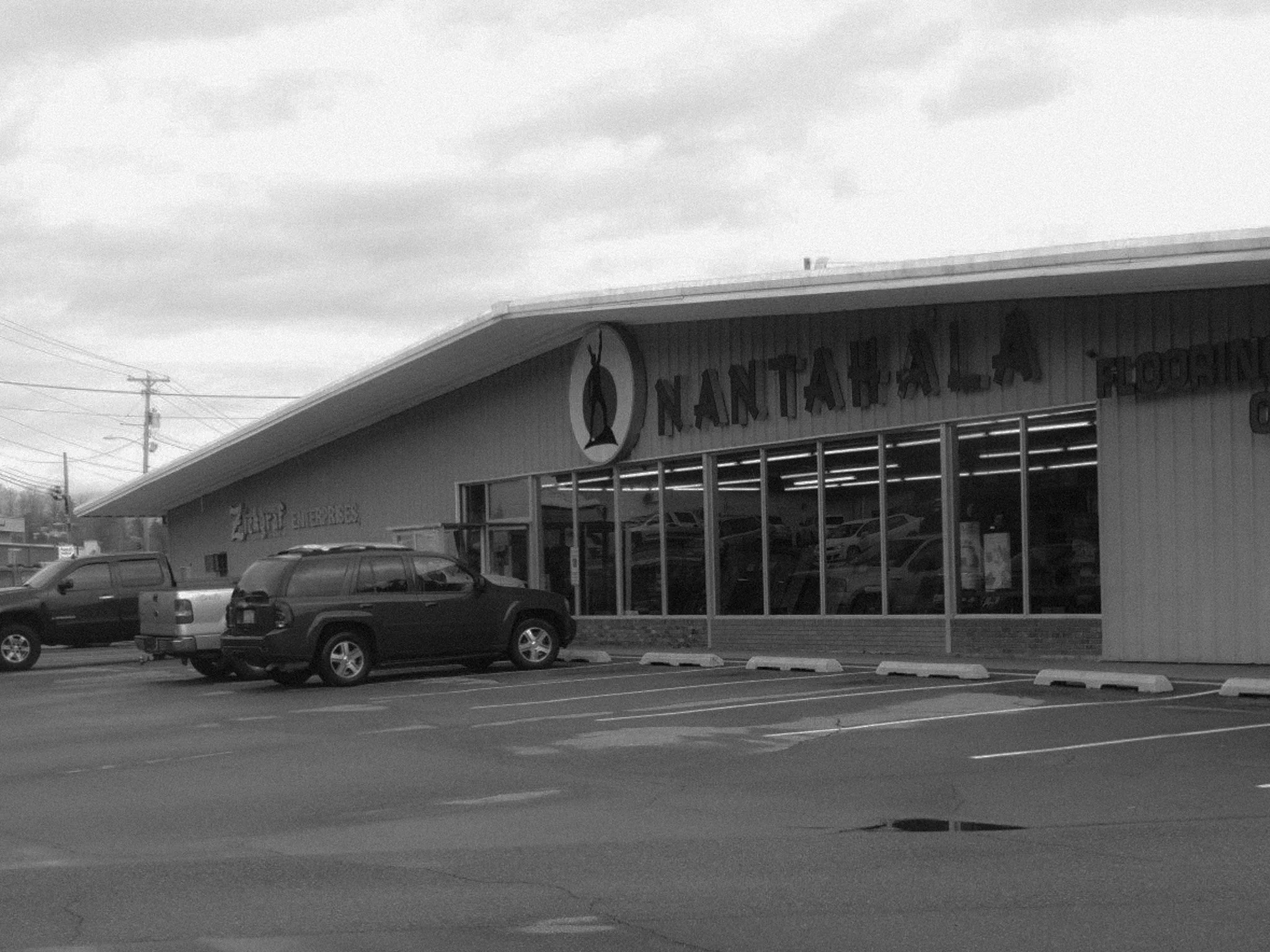 A parking lot in front of a store named NANTAHALA FLOORING with parked vehicles and large windows displaying cars inside.