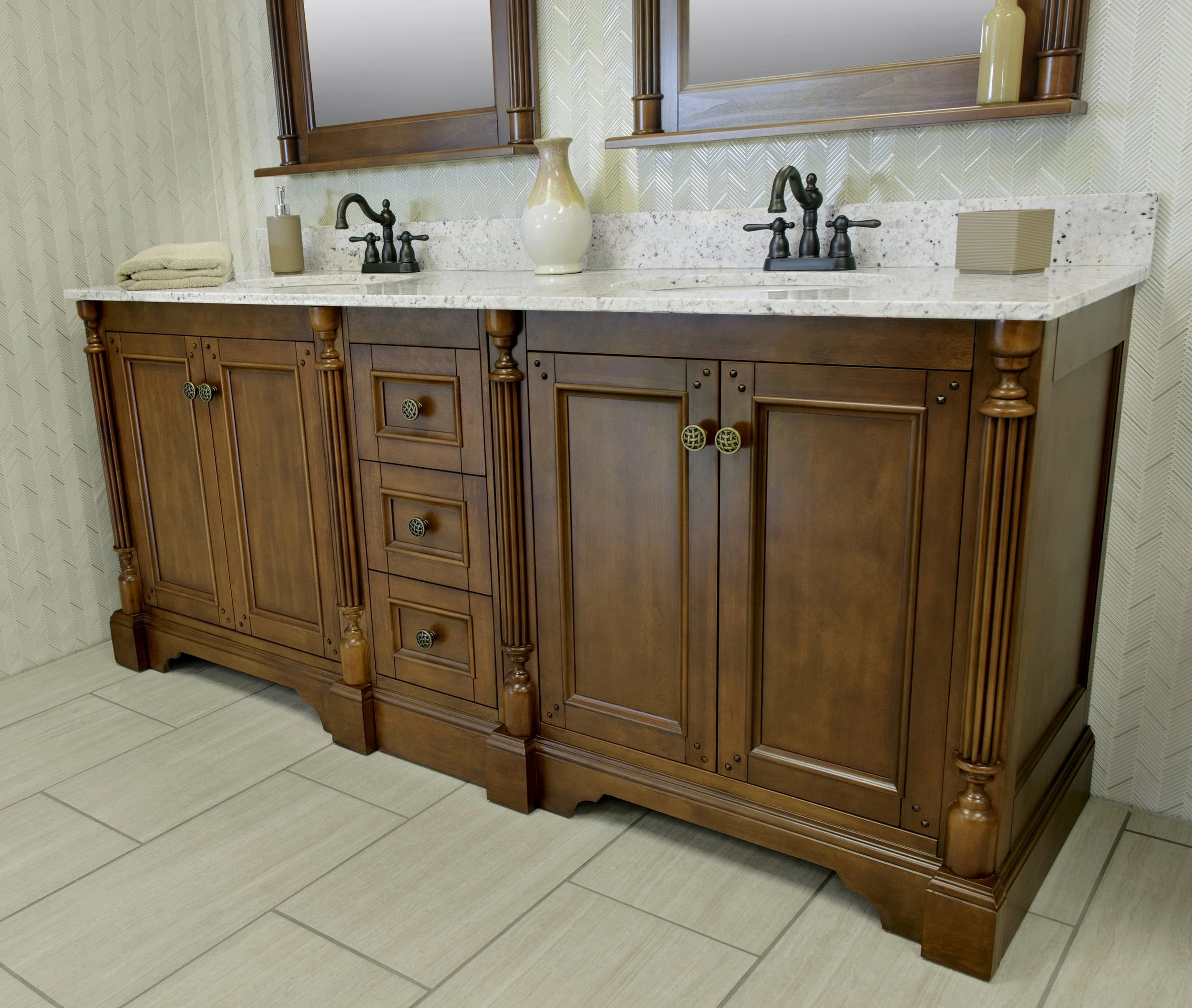 Traditional wooden bathroom vanity with a marble countertop, two sinks with black faucets, a beige towel, a soap dispenser, a decorative vase, mirror cabinets, and beige tiles on the floor.