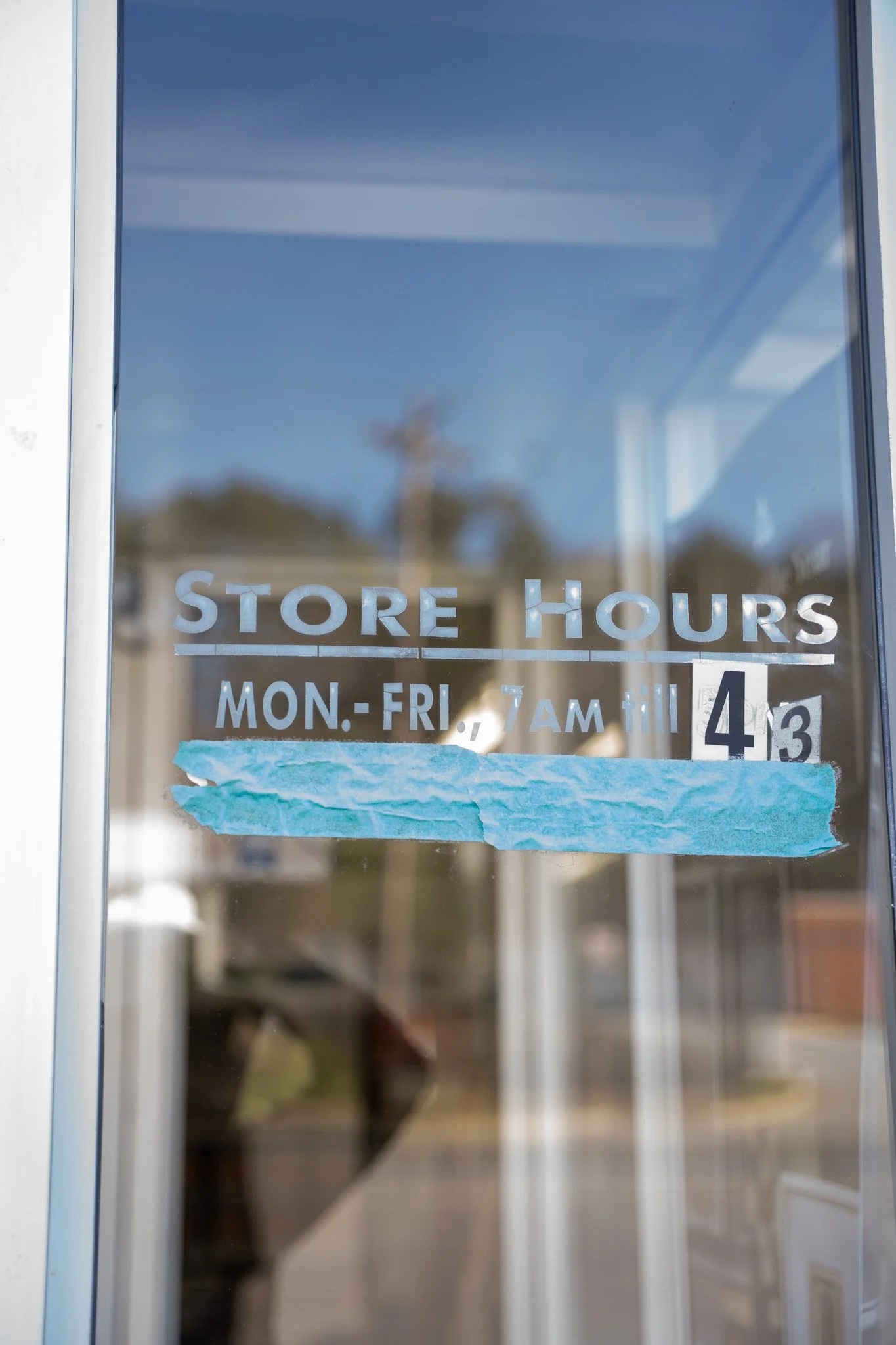 Store hours notice on glass door, indicating the store is open Monday to Friday from 7 am till 4:30 pm, the text is partially covered by a torn piece of blue paper.