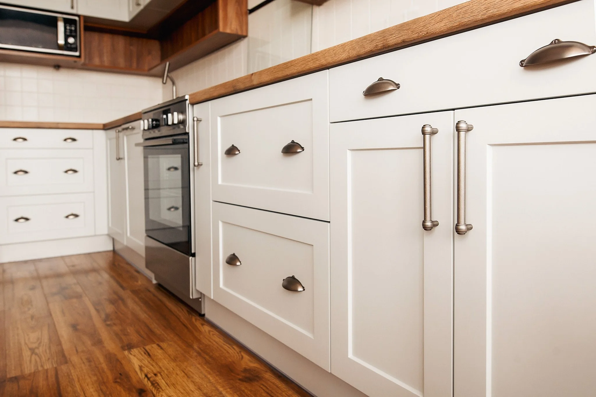 Kitchen with white cabinets, wooden countertops, a stainless steel oven, and wooden flooring.