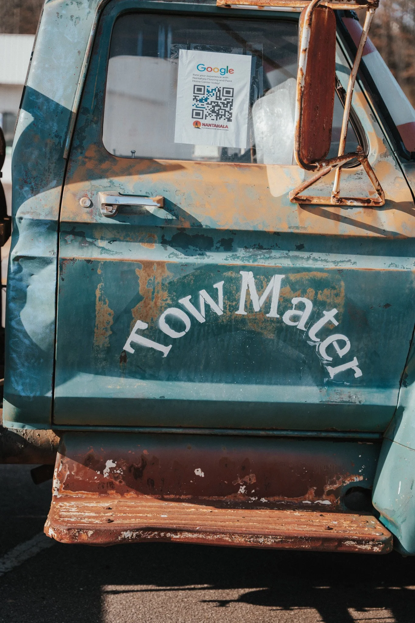 Close-up of an old, weathered truck with a sign in the window that has a QR code, Google logo, and the words 'Rate your experience with Nantahala' and 'Home Center'.
