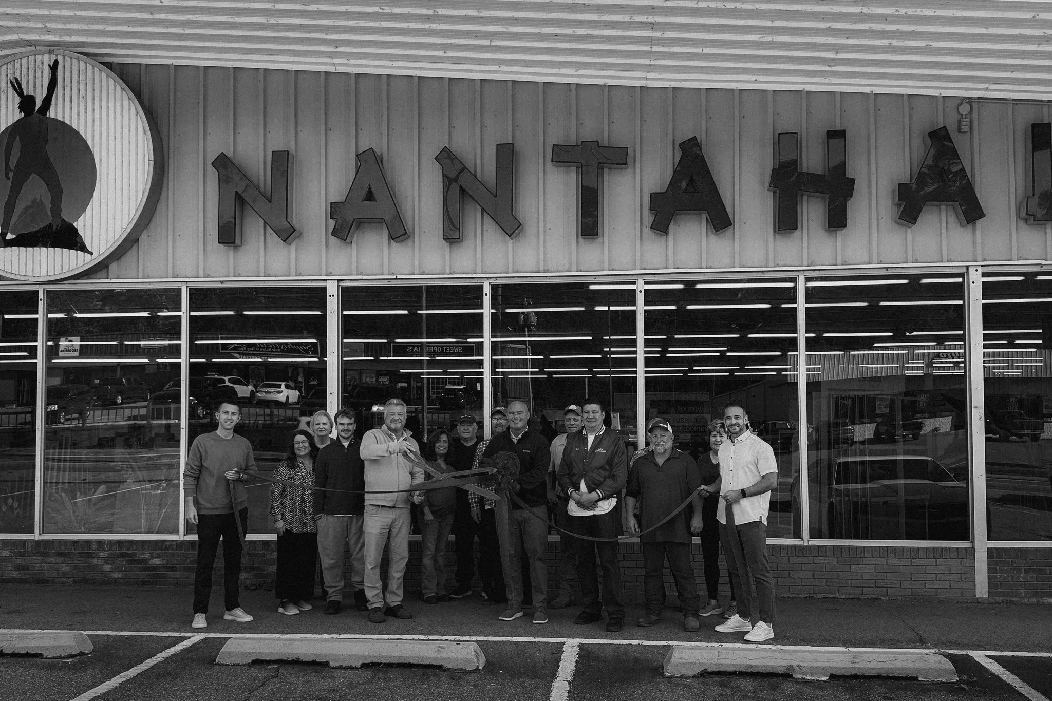 Group of people gathered outside NANTAH exit, participating in a ribbon-cutting ceremony in front of a store with large glass windows and a sign reading NANTAH.