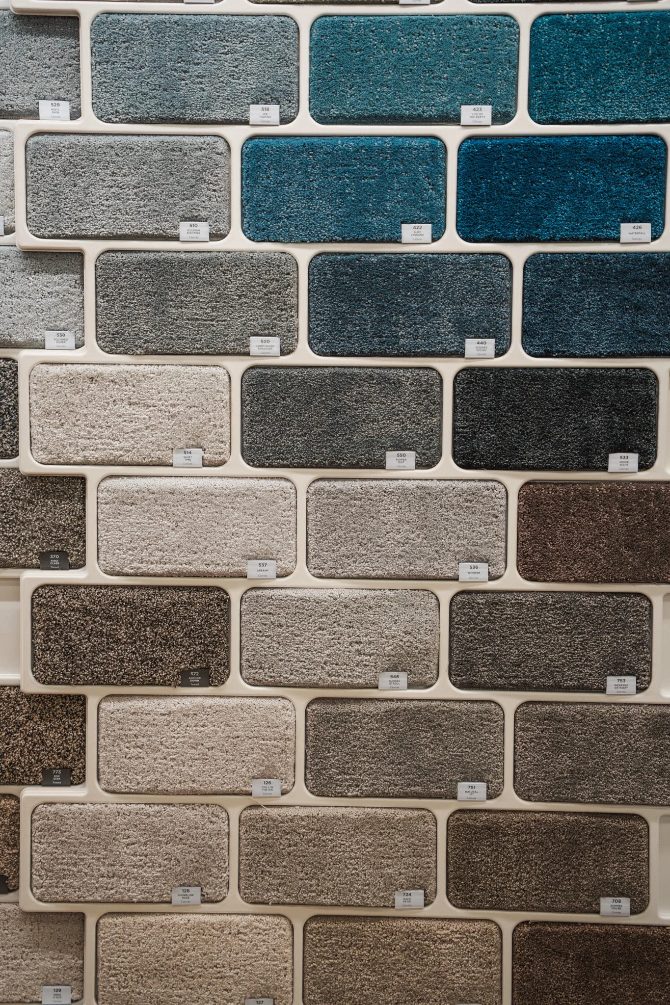 A display wall of carpet samples in various shades of blue, gray, and beige, each labeled with a small tag.