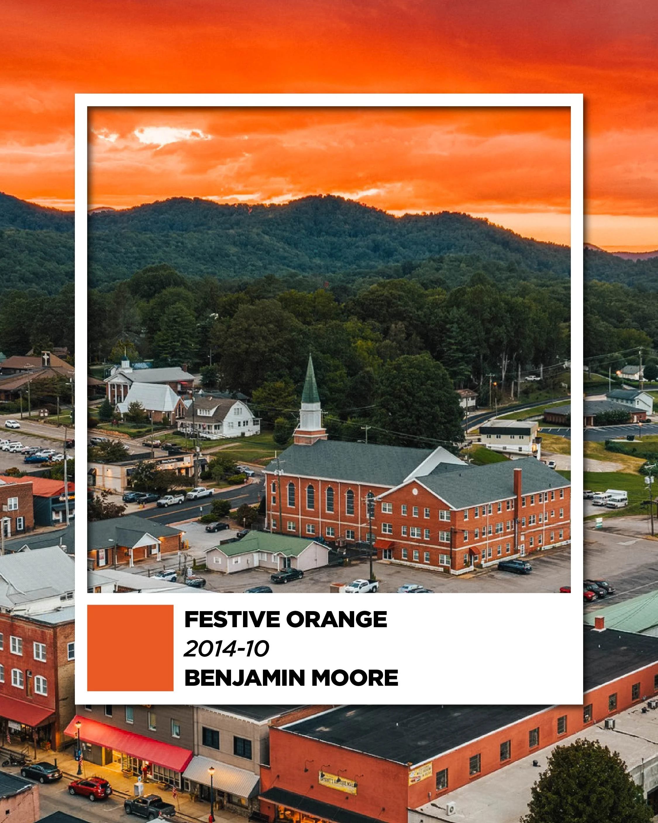 Sunset over a small town with a church surrounded by trees and mountains in the background.