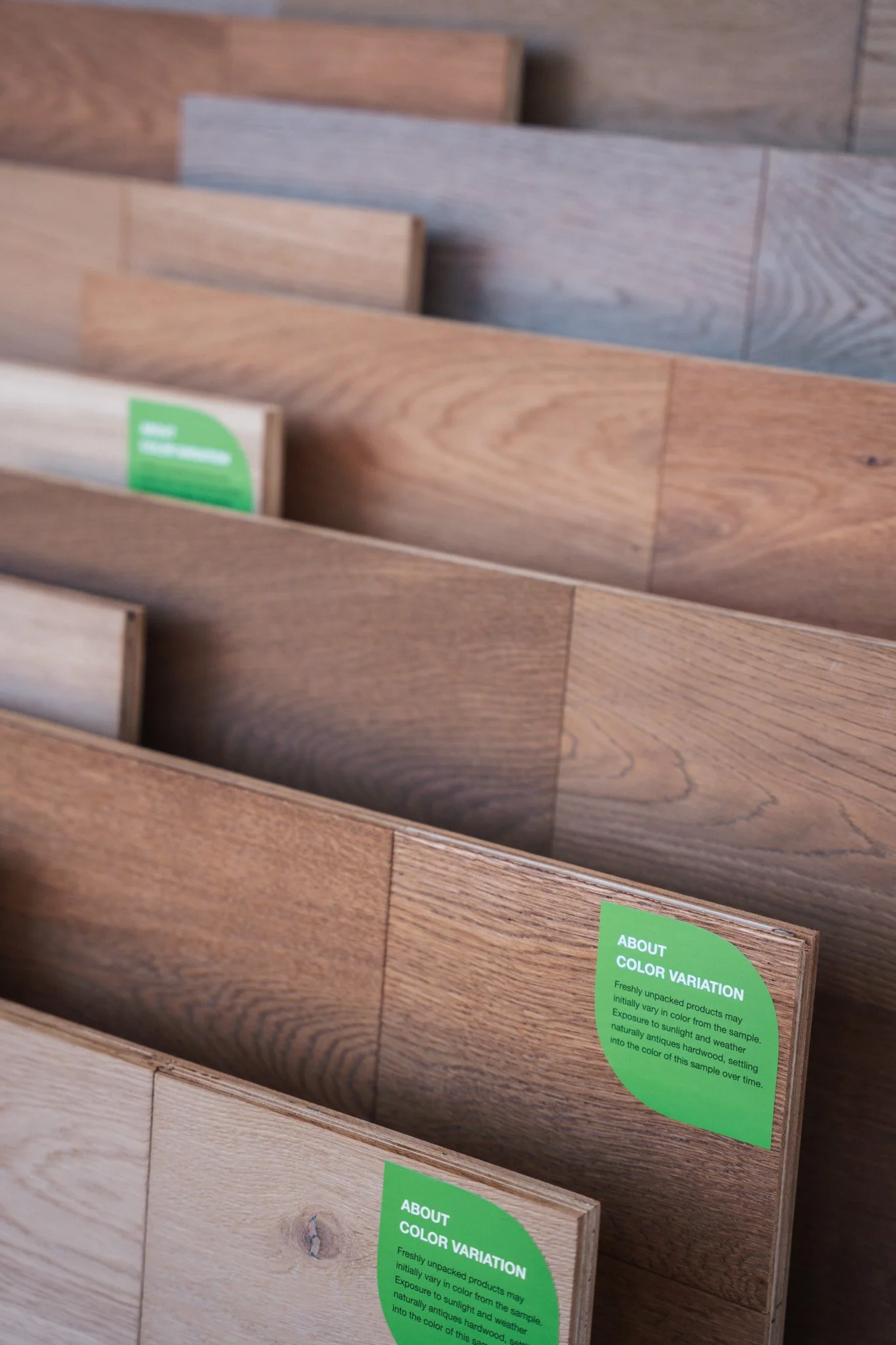 Close-up of several wooden floor samples with green informational labels about color variation.