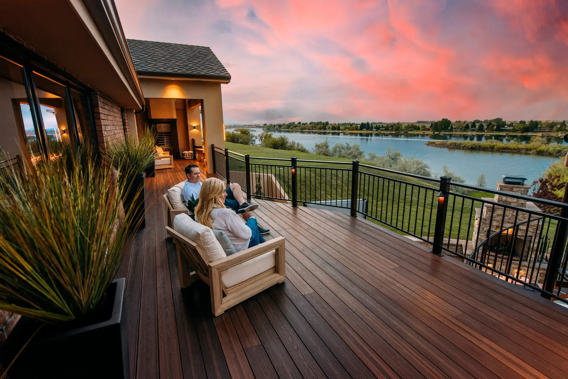 People relaxing on a wooden deck overlooking a river at sunset