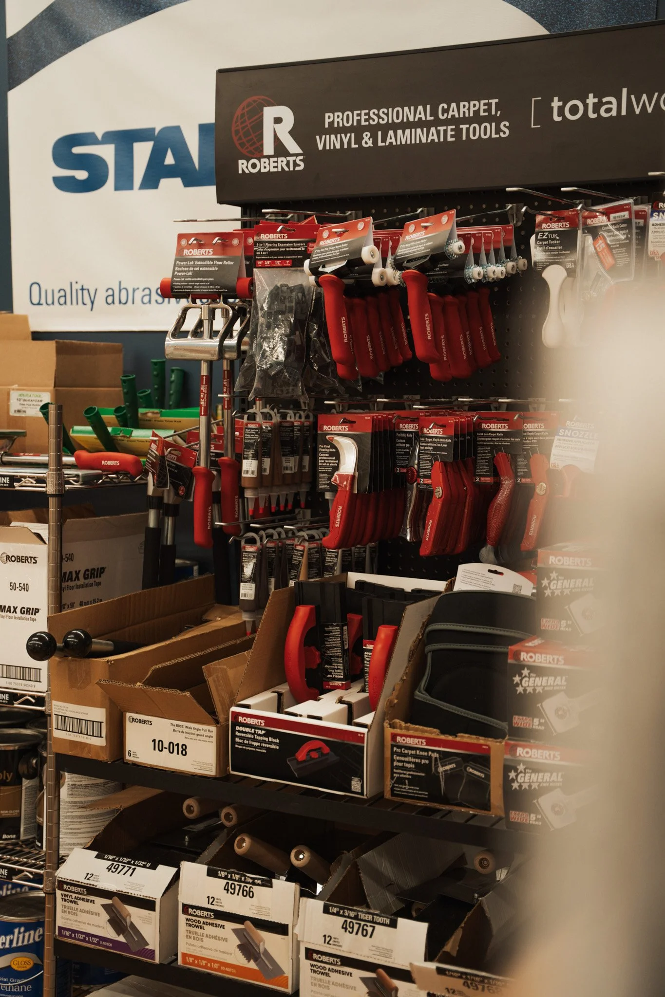 Display of Roberts branded tools including scrapers, tapes, and adhesives in a hardware store.