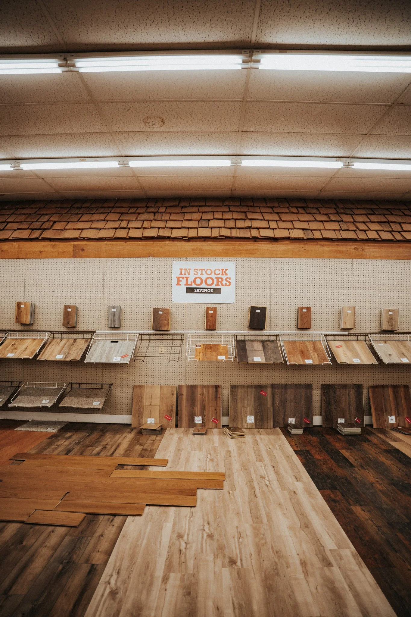 Display of various flooring samples in a store, with a sign reading 'In Stock Floors' and 'Savings' above them.