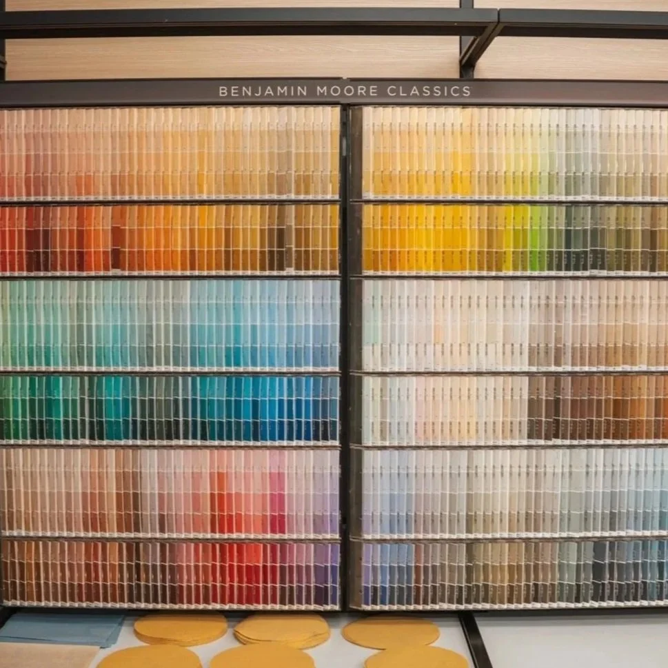A large display shelf of Benjamin Moore paint color samples organized by color, including shades of red, orange, yellow, green, blue, purple, and neutrals.