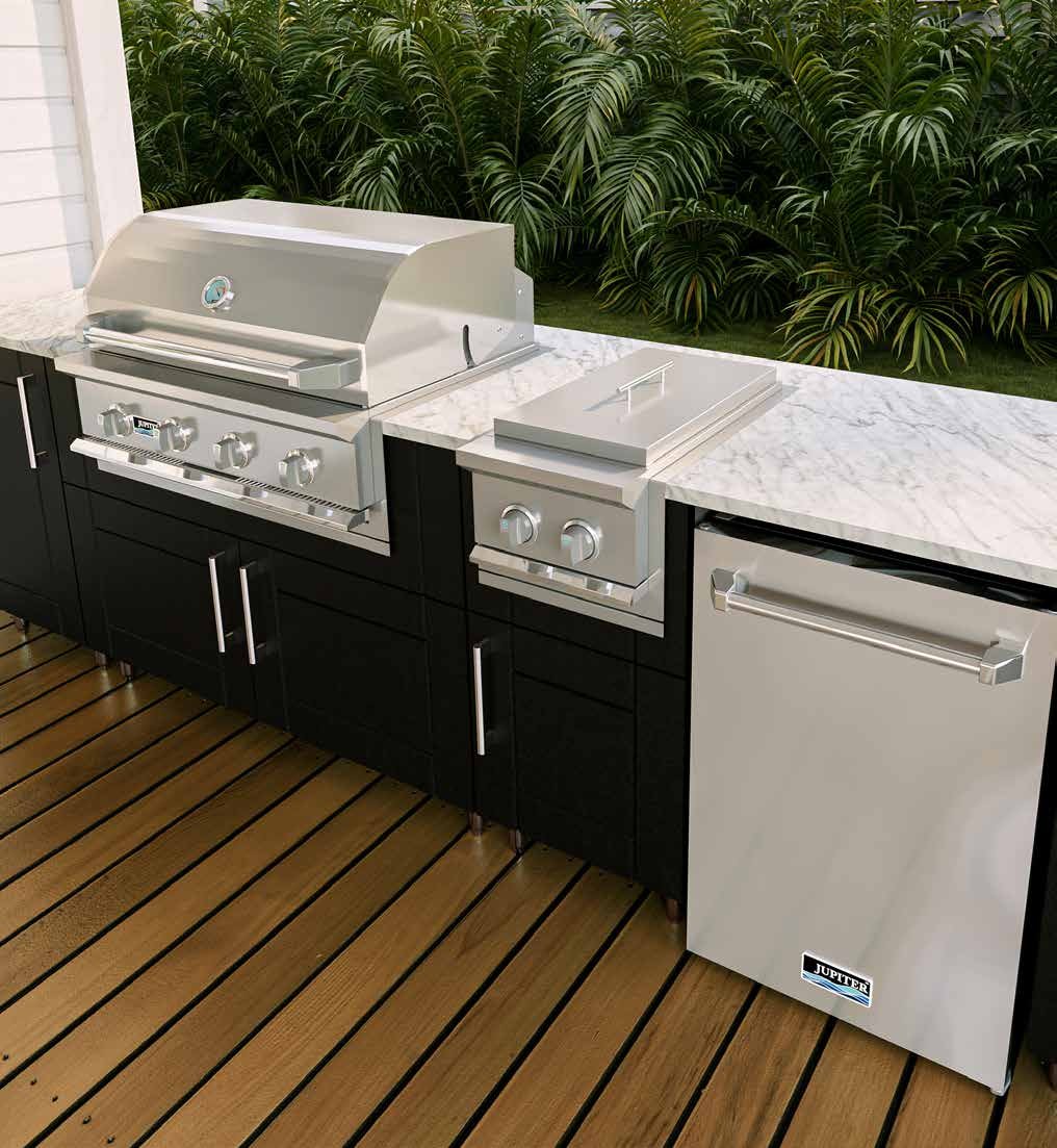 Outdoor kitchen with a black cabinet under a white marble countertop, featuring a silver grill, a small griddle, and a mini fridge, with greenery in the background and a wooden deck floor.
