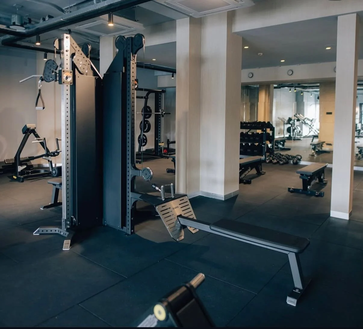 Empty gym with workout equipment including a weight machine, benches, dumbbells, and weights on racks.