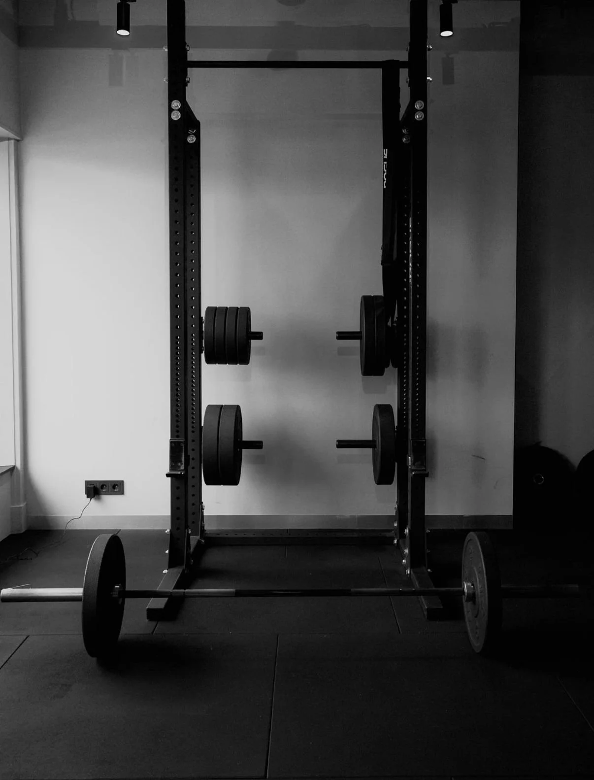Empty gym gym squat rack with weights and a barbell on the floor.