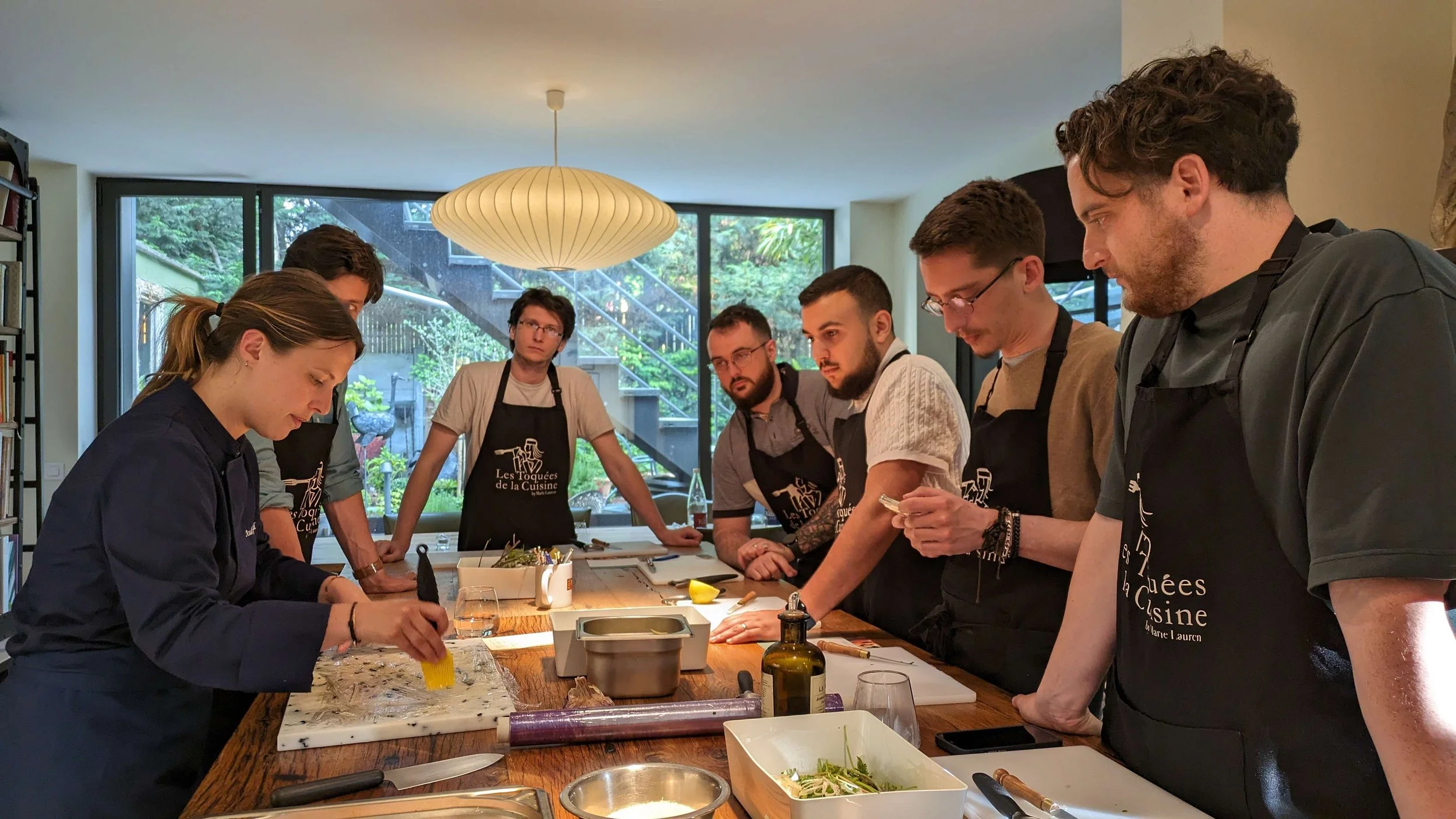 Un atelier cuisine a été organisé pour l'ensemble de nos ikiviens lillois pour un afterwork. Nos collaborateurs sont autour d'un ilot et observent la cheffe.
