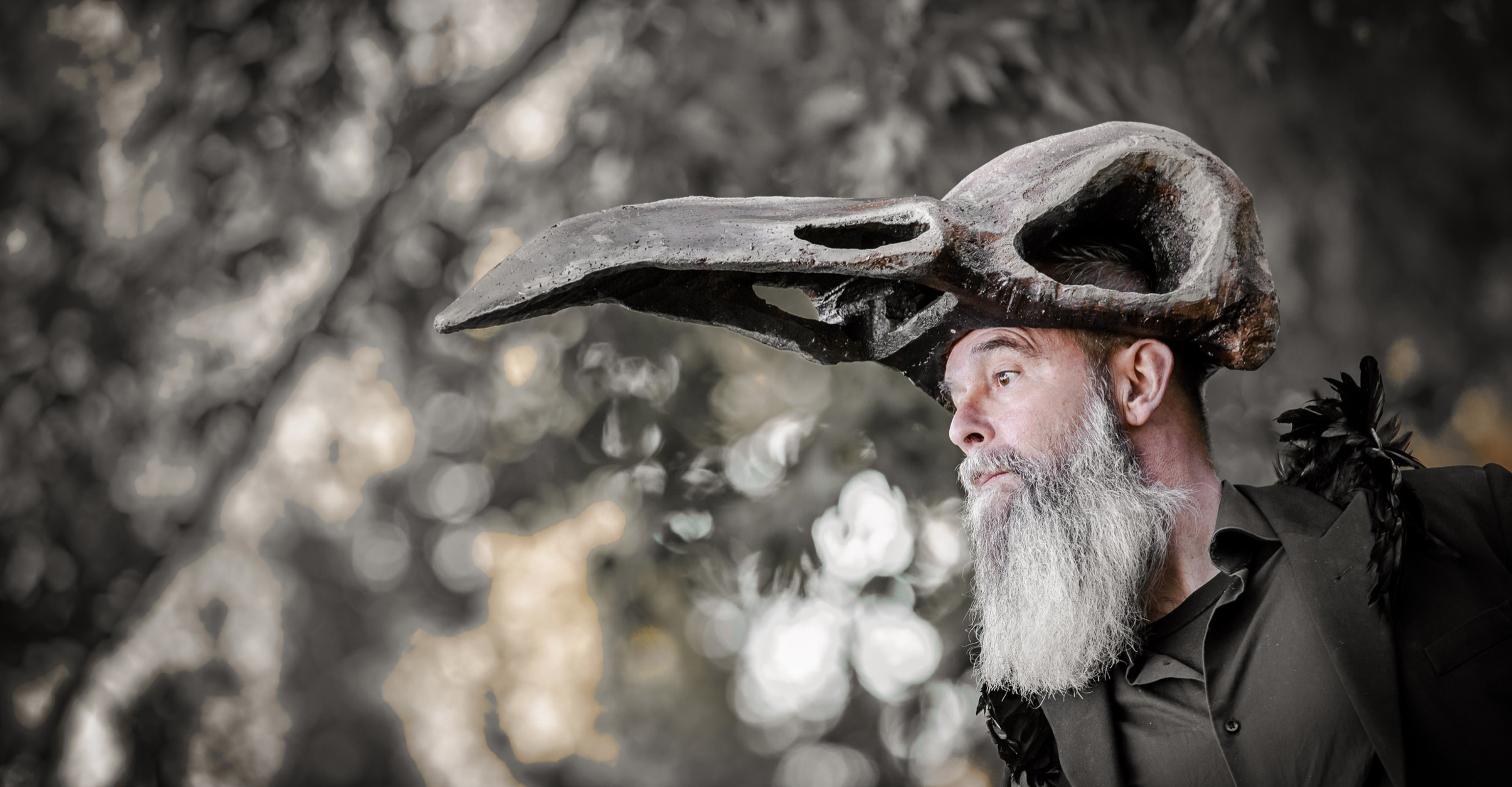 Man met een grote vogelskullenkostuum op zijn hoofd, zittend in een boom.