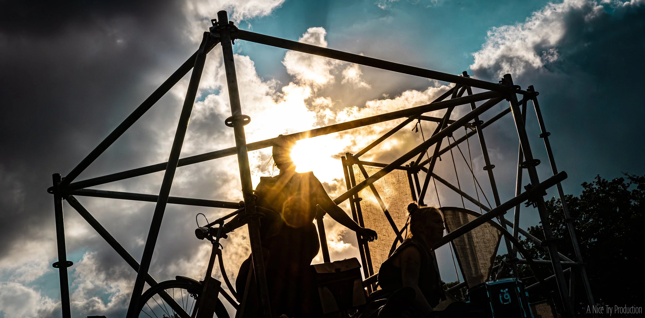 Silhouetten van mensen op een speelstructuur tijdens zonsondergang met een bewolkte hemel.