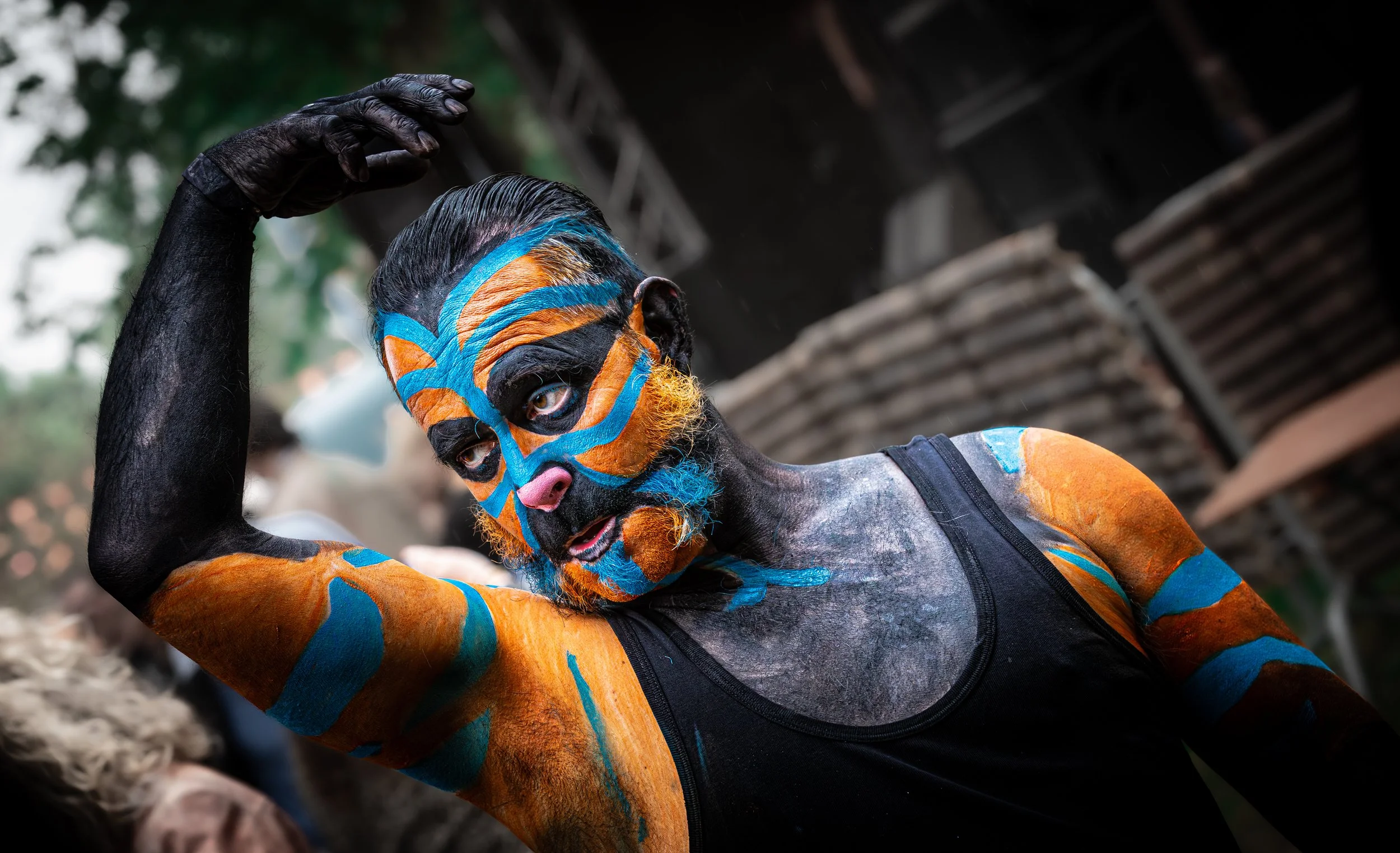 Man met gezicht en armen geschilderd in oranje, blauw en zwart, in een zwart shirt, buiten.