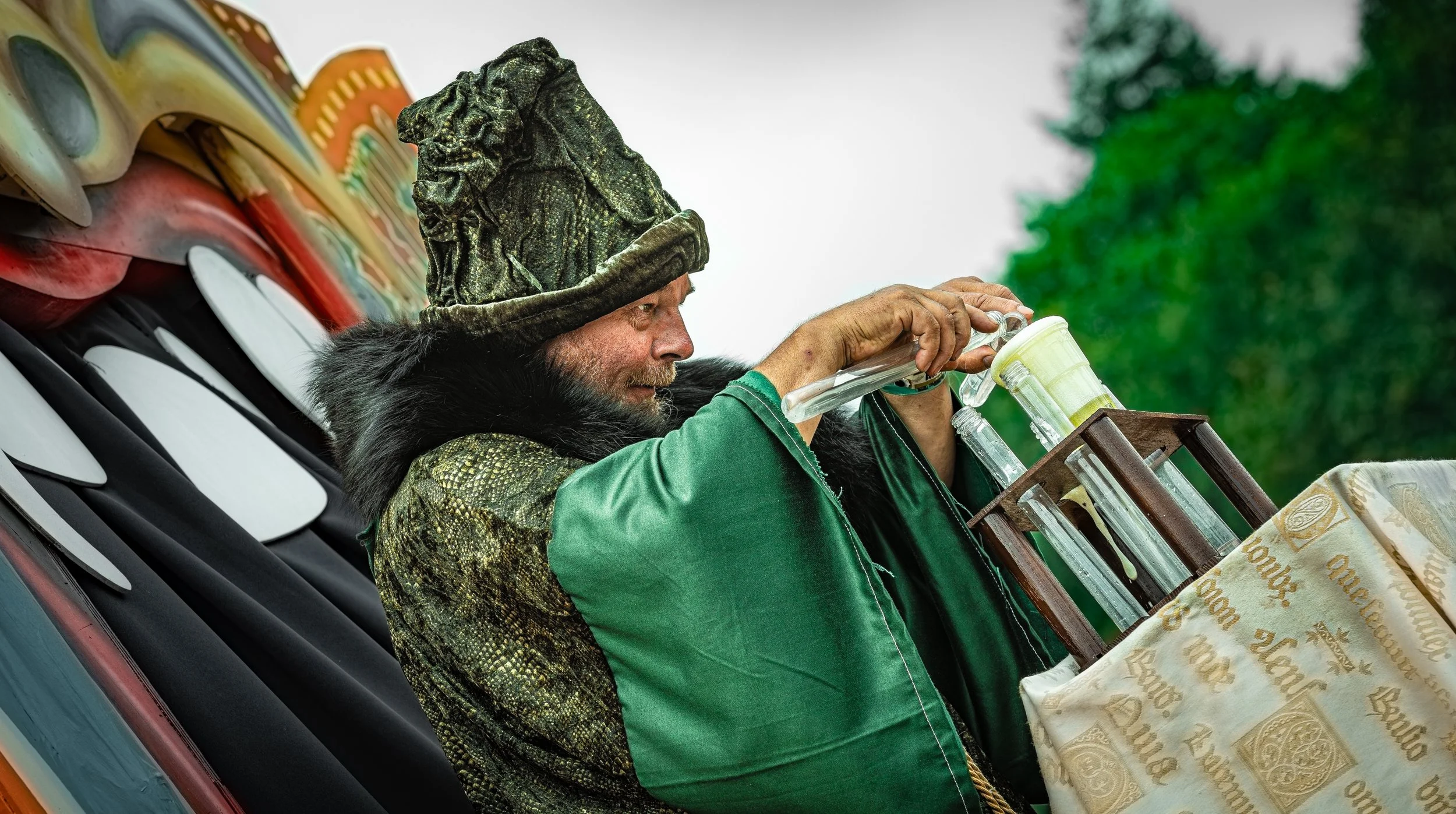 Man in klederdracht en hoed mixt verschillende vloeistoffen met elkaar.