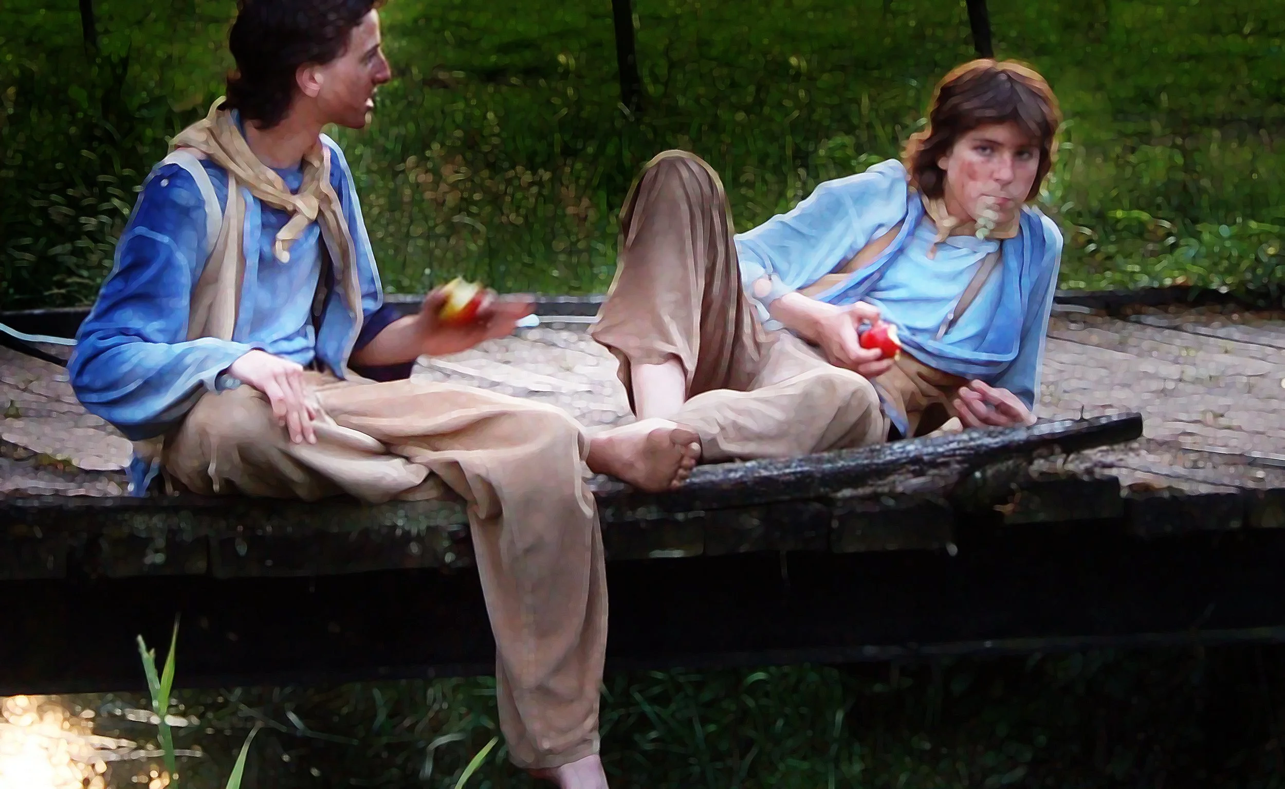 Twee jonge mannen liggen op een houten brug, vieren picknick met fruit en dragen historische kledij, omgeven door groen bos.