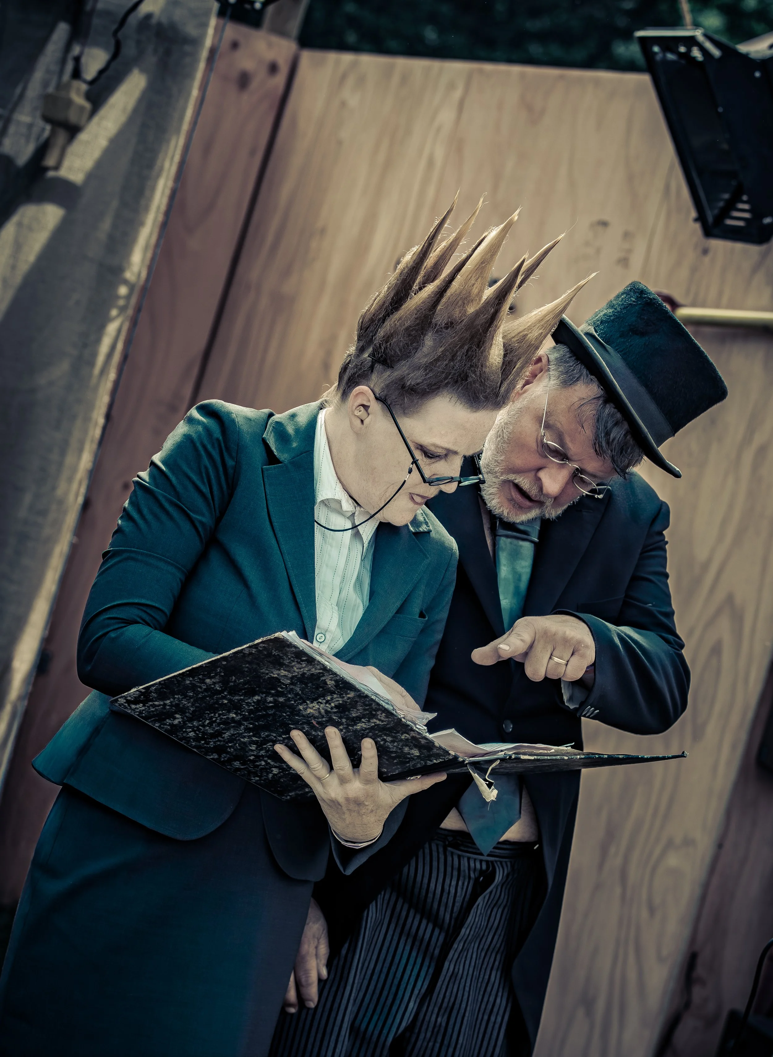Twee mensen in kostuums kijken samen naar een oud boek in een houten decor.