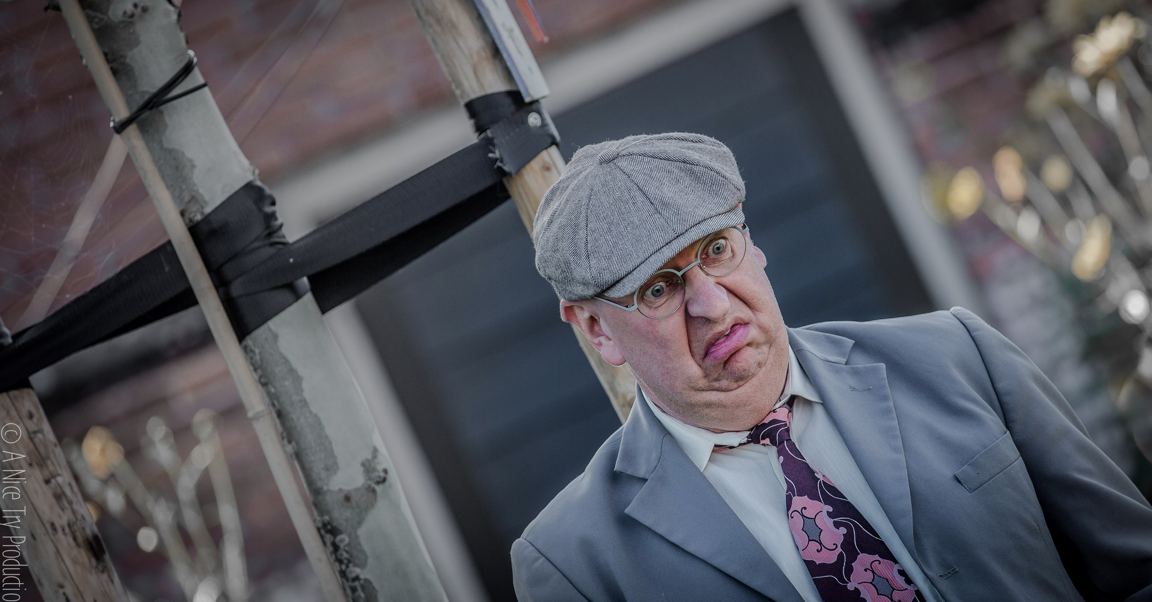 Man met een grijze hoed, bril en nette pak, met een verwarde uitdrukking op gezicht.