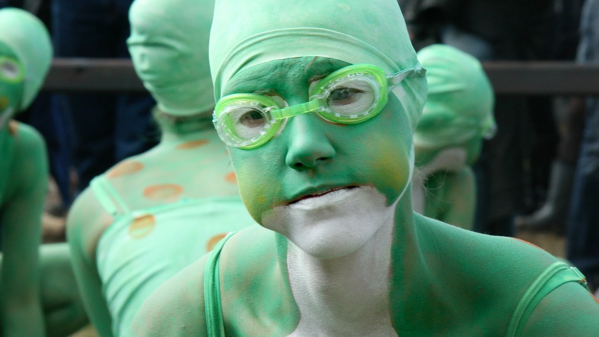 Persoon met groene body paint, zwembril en wit gezichtsmake-up, mogelijk bij een performance of evenement.
