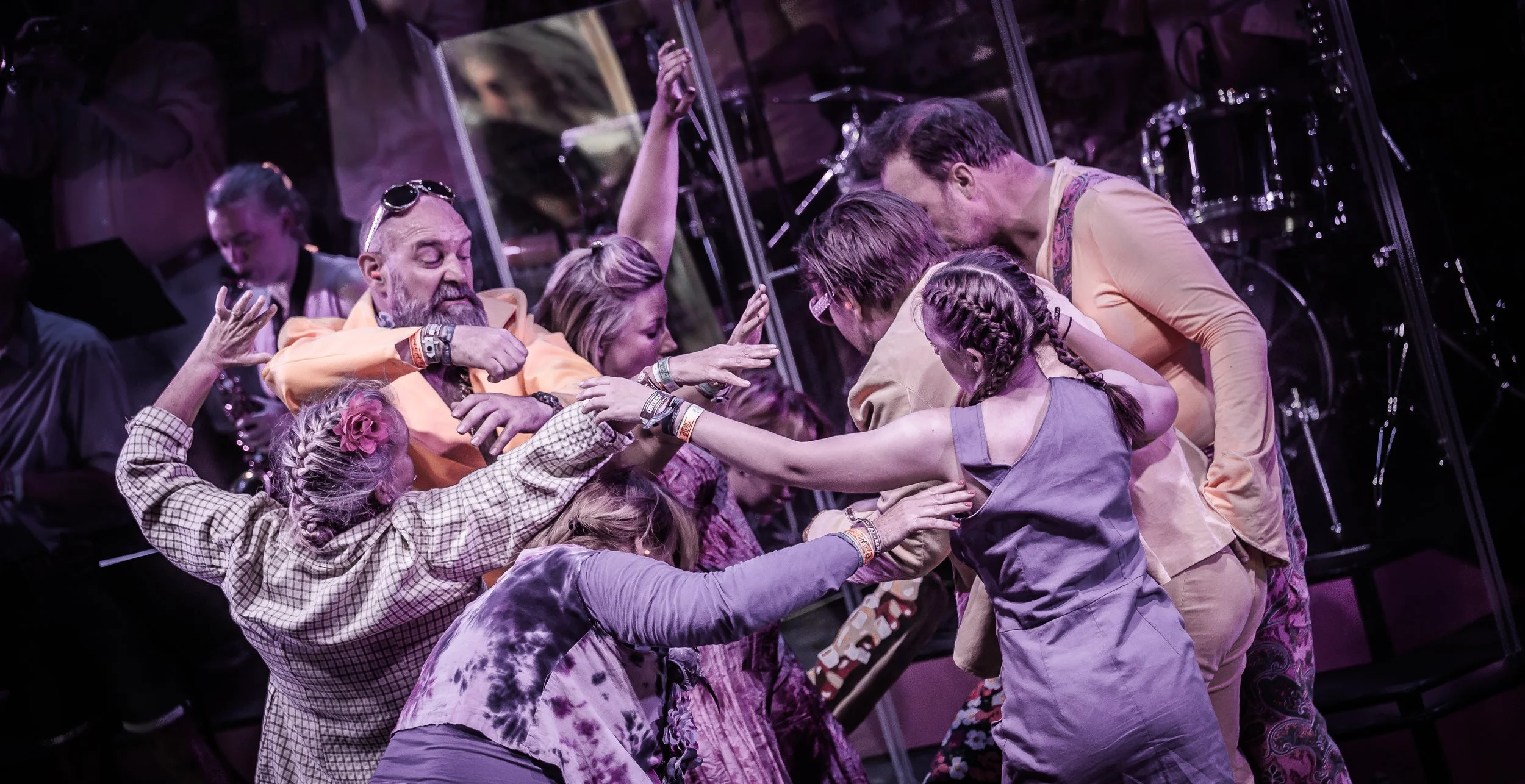 Mensen in een discussie op een podium of theater, met een driekoppige band op de achtergrond.
