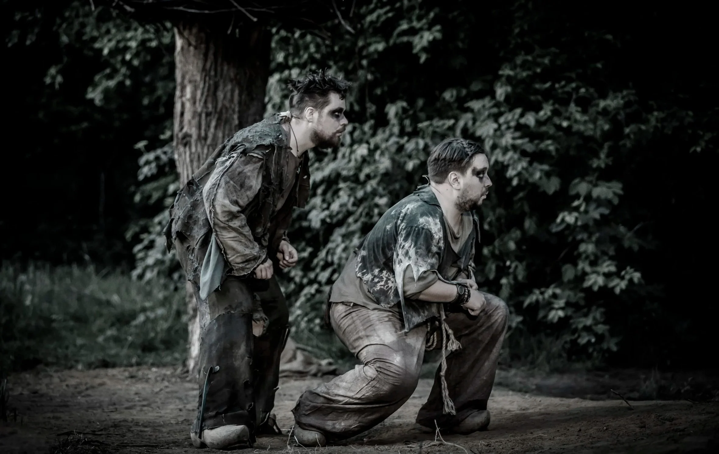 Twee jonge mannen knielen in een bos, gekleed in camouflagekleding en zien er uitgeput uit.