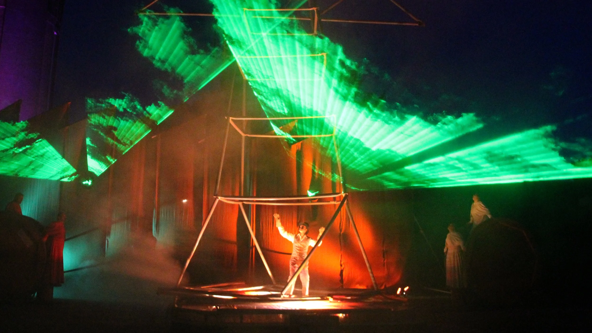 Optische illustratie met groene laserstralen, een persoon in oranje pakken onder een attractie, en andere mensen op de achtergrond, kleurrijk verlicht in een donkere setting.