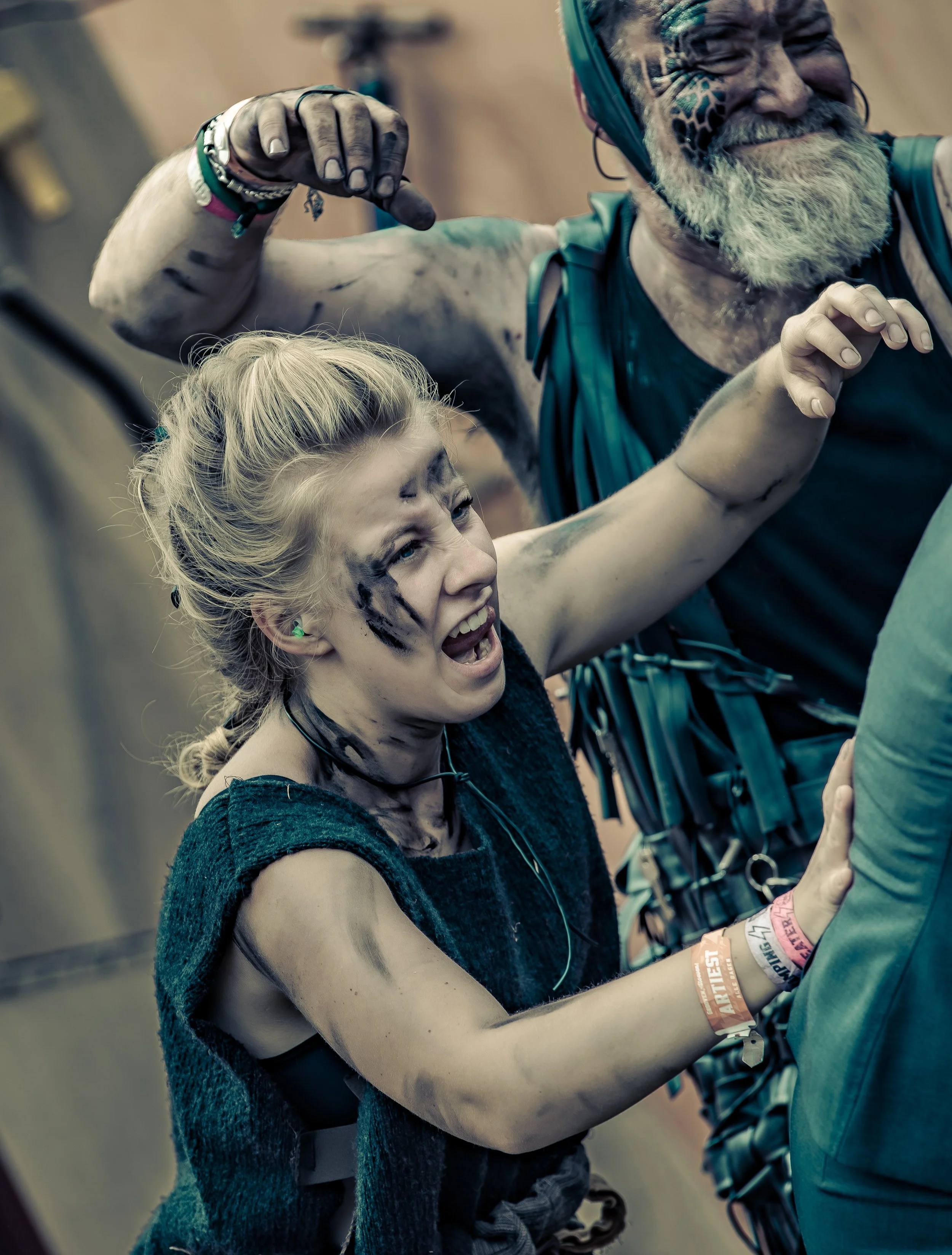 Twee jongeren op een festival, bedekt met modder. Ze lijken te genieten en maken plezier, met een energieke houding en uitdrukking.