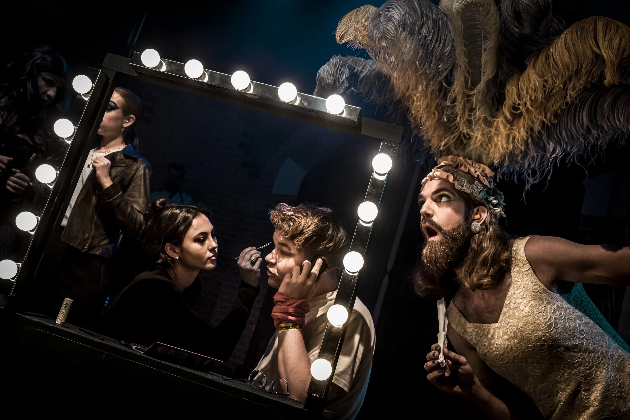 Mensen die zich voorbereiden voor een optreden bij een spiegel met lampen, in een donkere setting.