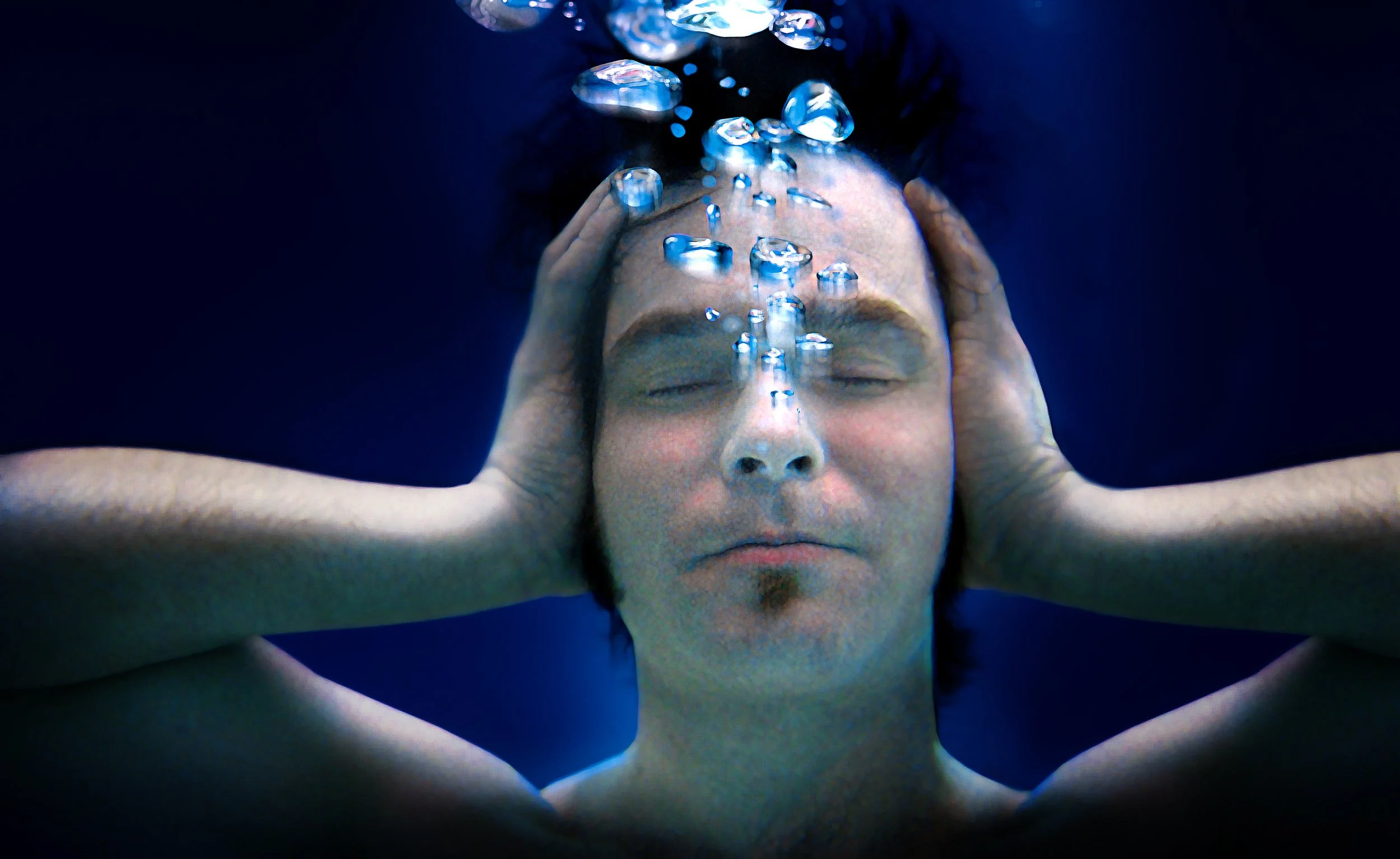 Man onder water met ogen dicht, handen op hoofd, luchtbellen opstijgend.