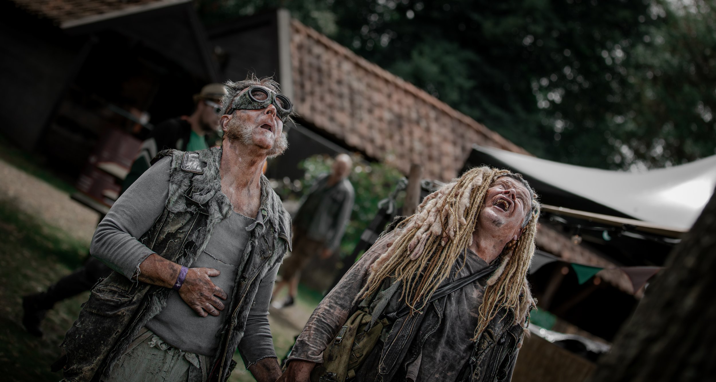 Twee mensen verkleed met versleten kleding en gezichtsmake-up bij een evenement in de buitenlucht.