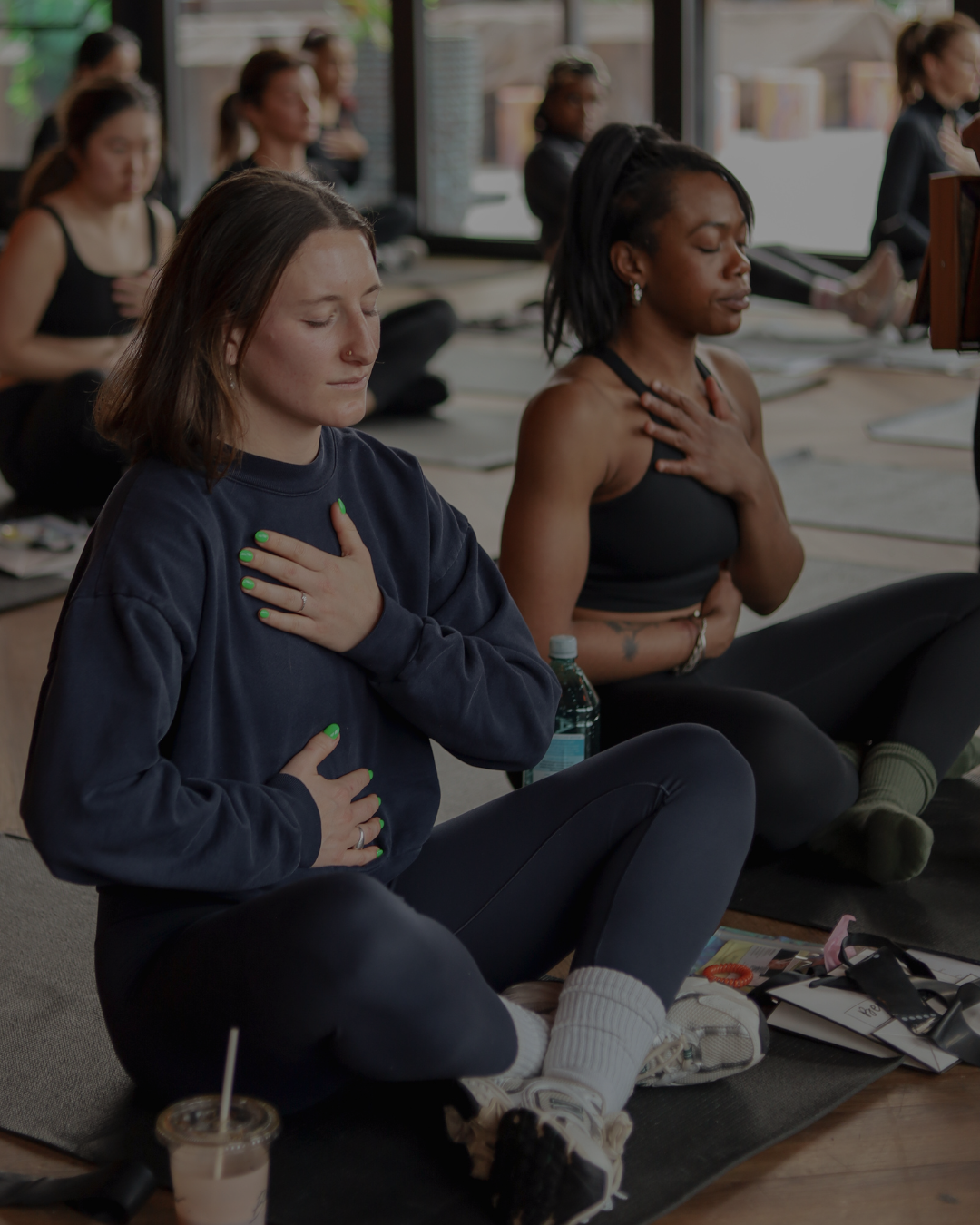 Women sitting on yoga mats in a meditation class with hands on their chests and eyes closed.