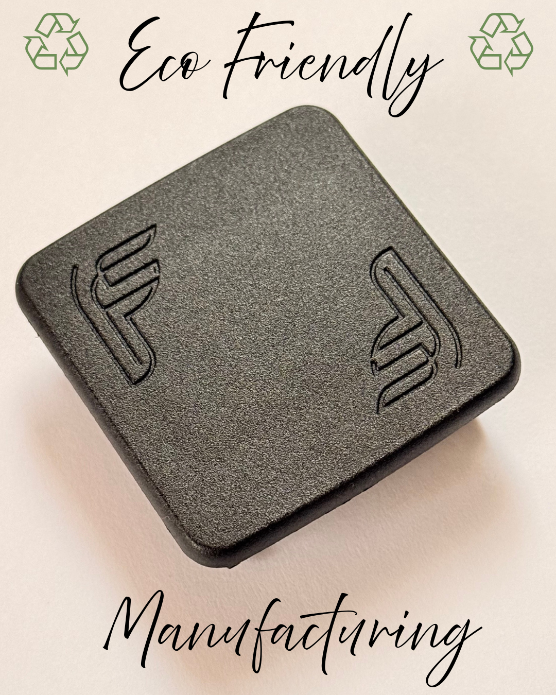 A black square object with a textured surface and symbols embossed on it, with text reading 'Eco friendly' at the top and 'Manufacturing' at the bottom, and green recycling symbols in the corners.