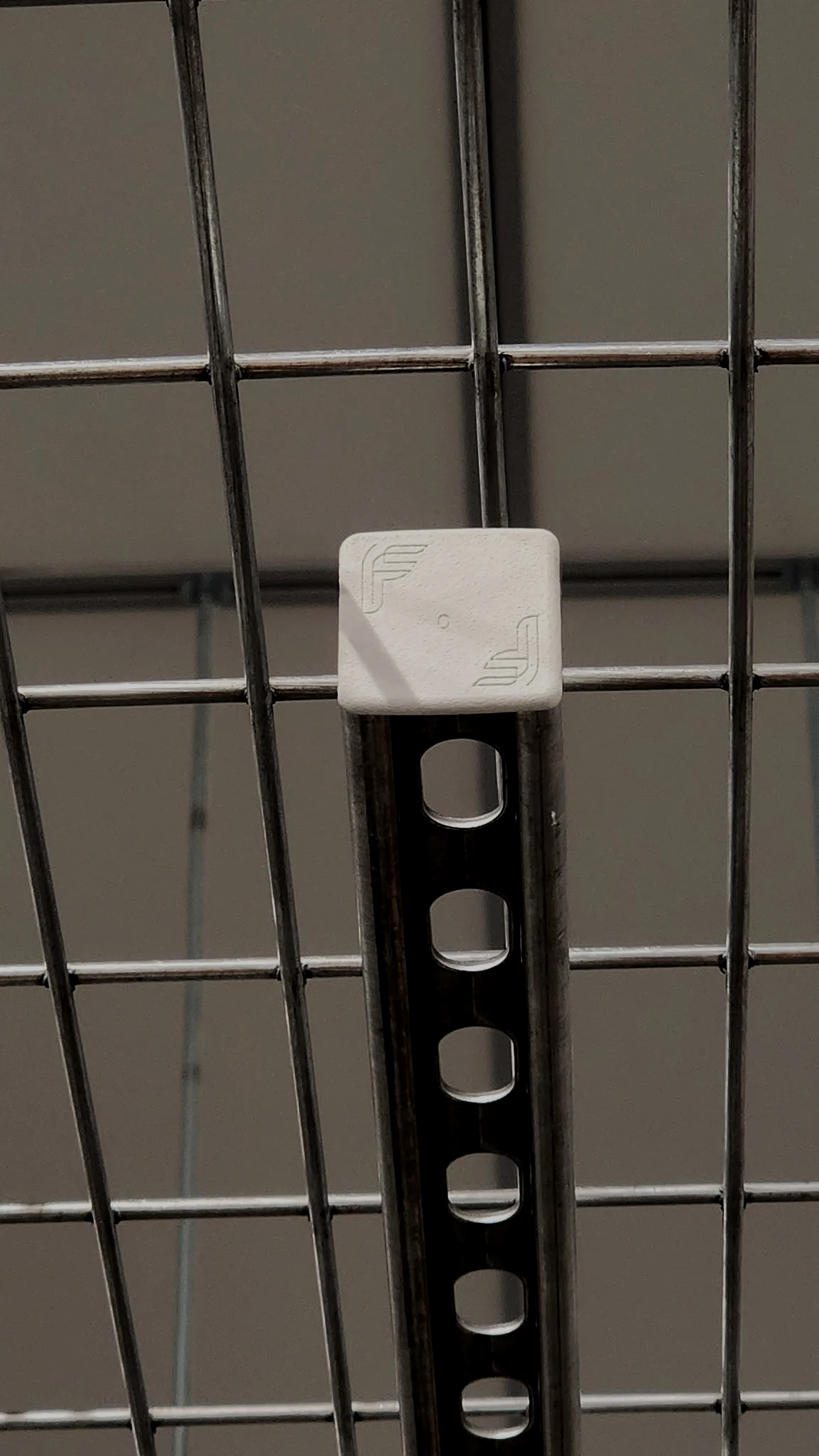 Close-up of a shopping cart wire grid with a white plastic clip attached to the metal support.