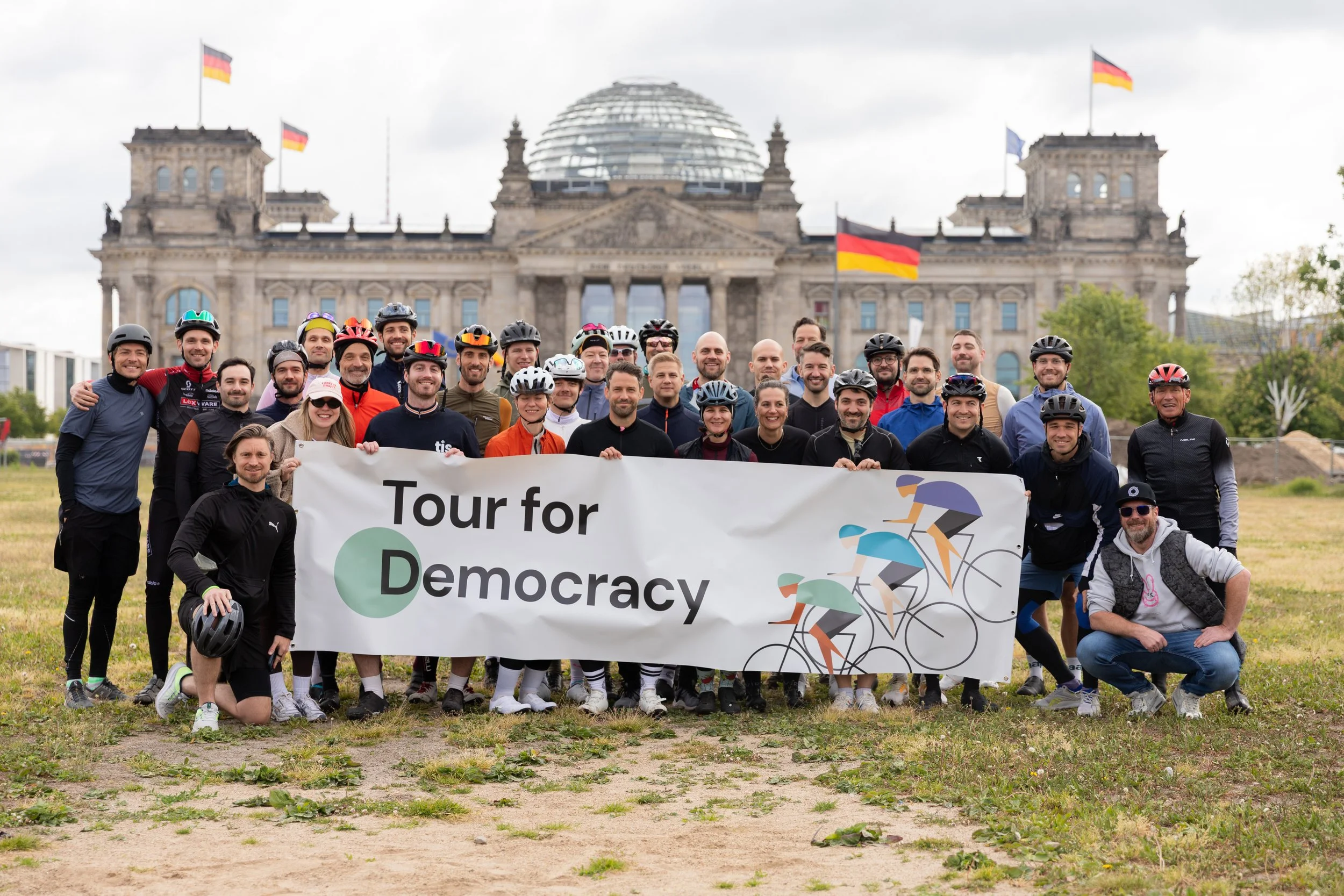 Gruppe von Menschen mit Helmen, die vor dem Reichstagsgebäude in Berlin ein Banner mit der Aufschrift "Tour for Democracy" halten.