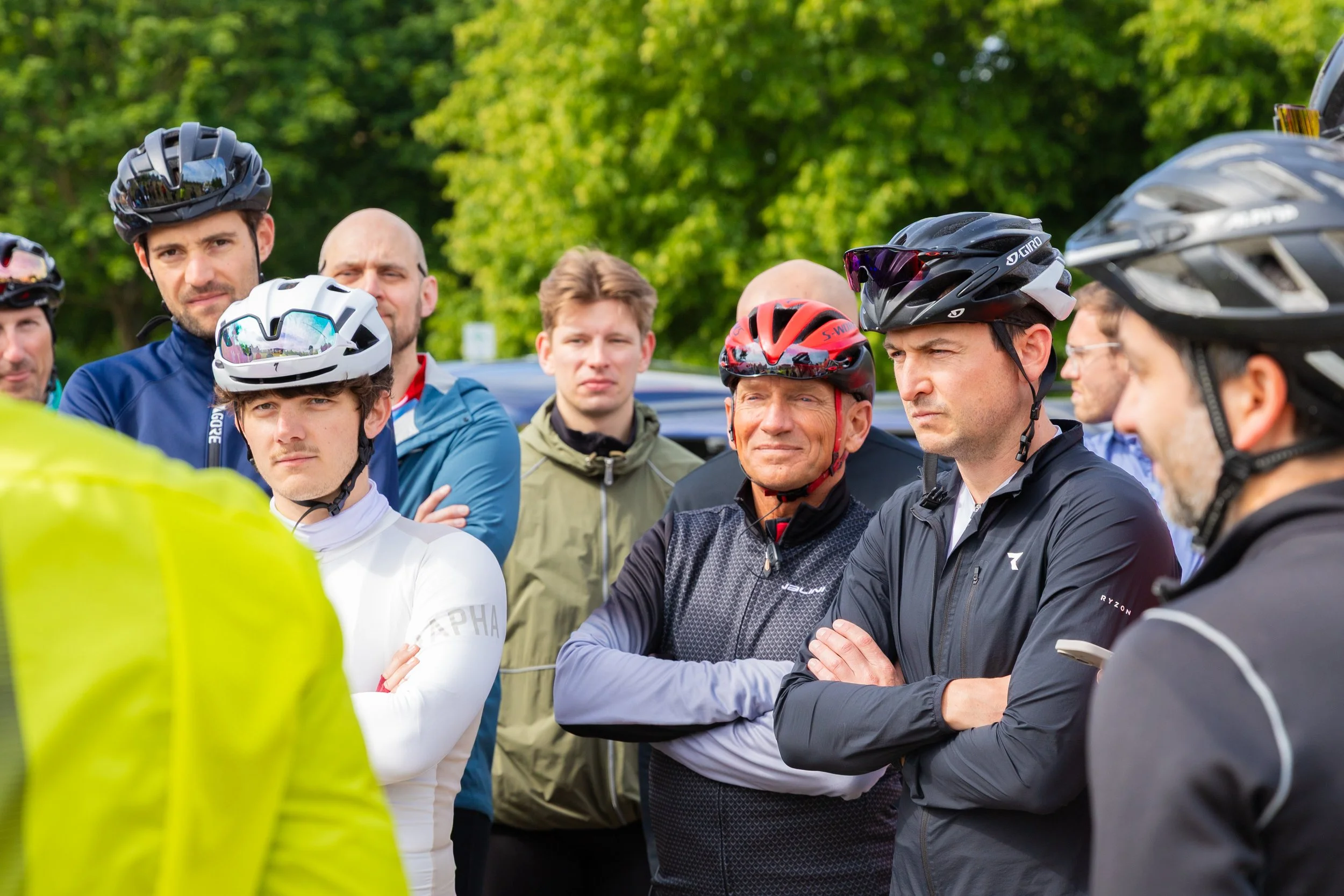 Gruppe von Radfahrern in Helmen, die sich im Freien versammelt haben und zuhören.