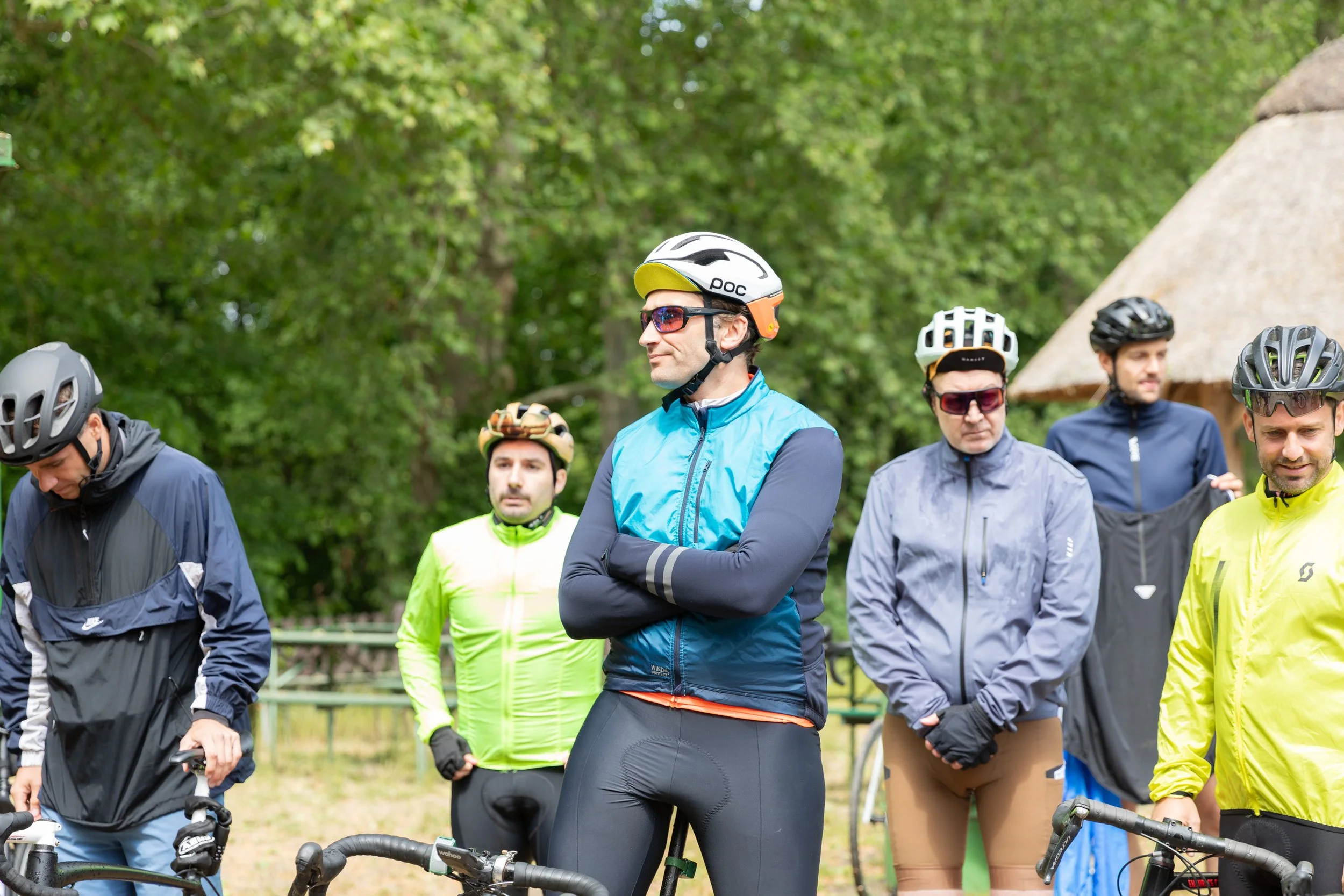 Eine Gruppe von Männern mit Fahrradhelmen und Fahrrädern steht im Freien mit grünen Bäumen im Hintergrund.