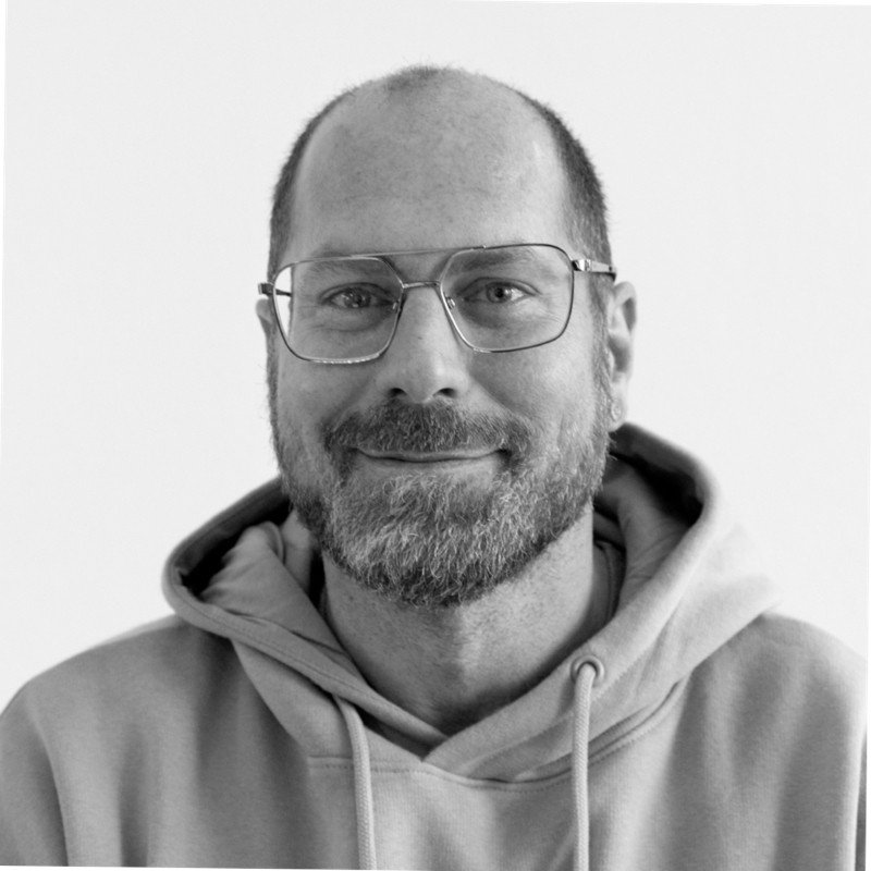 Mann mit Brille, Vollbart, trägt Hoodie, lächelt, schwarzes und weißes Foto