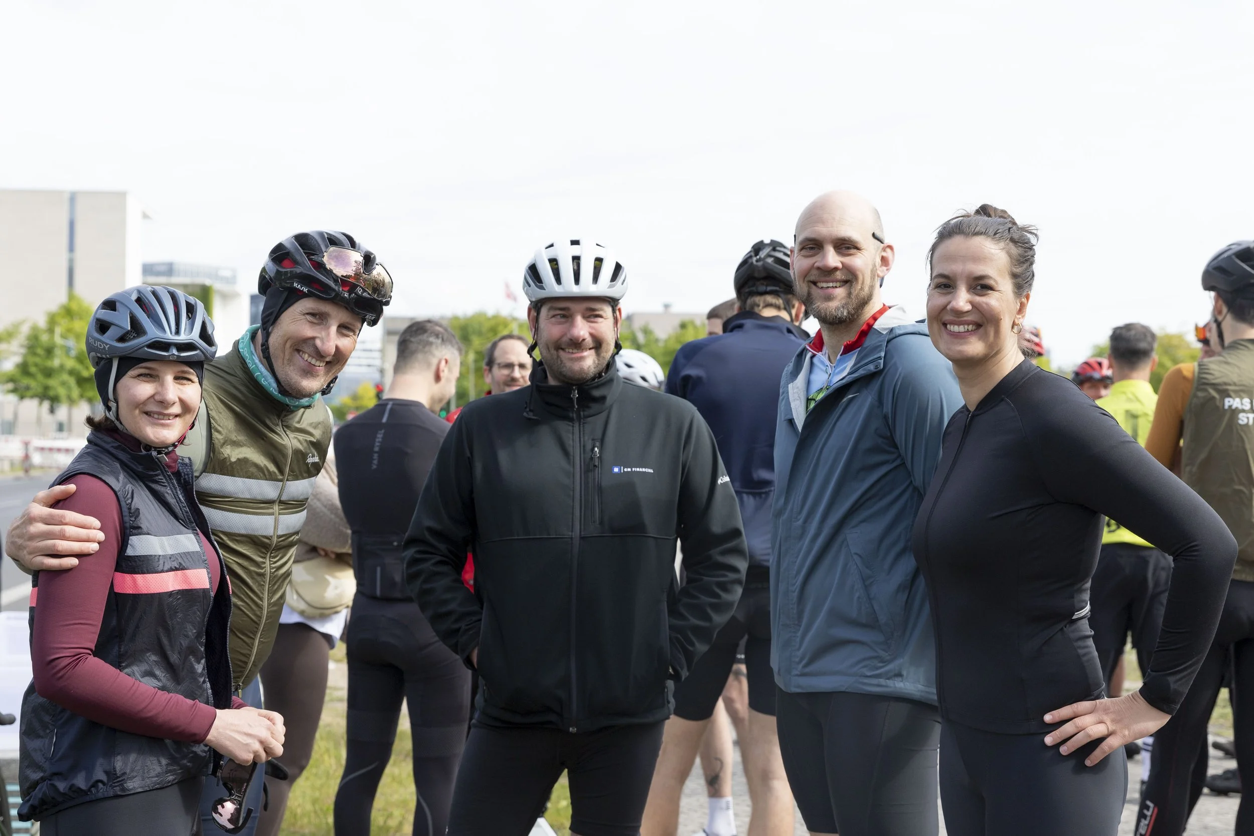 Fünf Personen tragen Fahrradhelme und Sportkleidung, stehen draußen in einer Gruppe und lächeln in die Kamera.