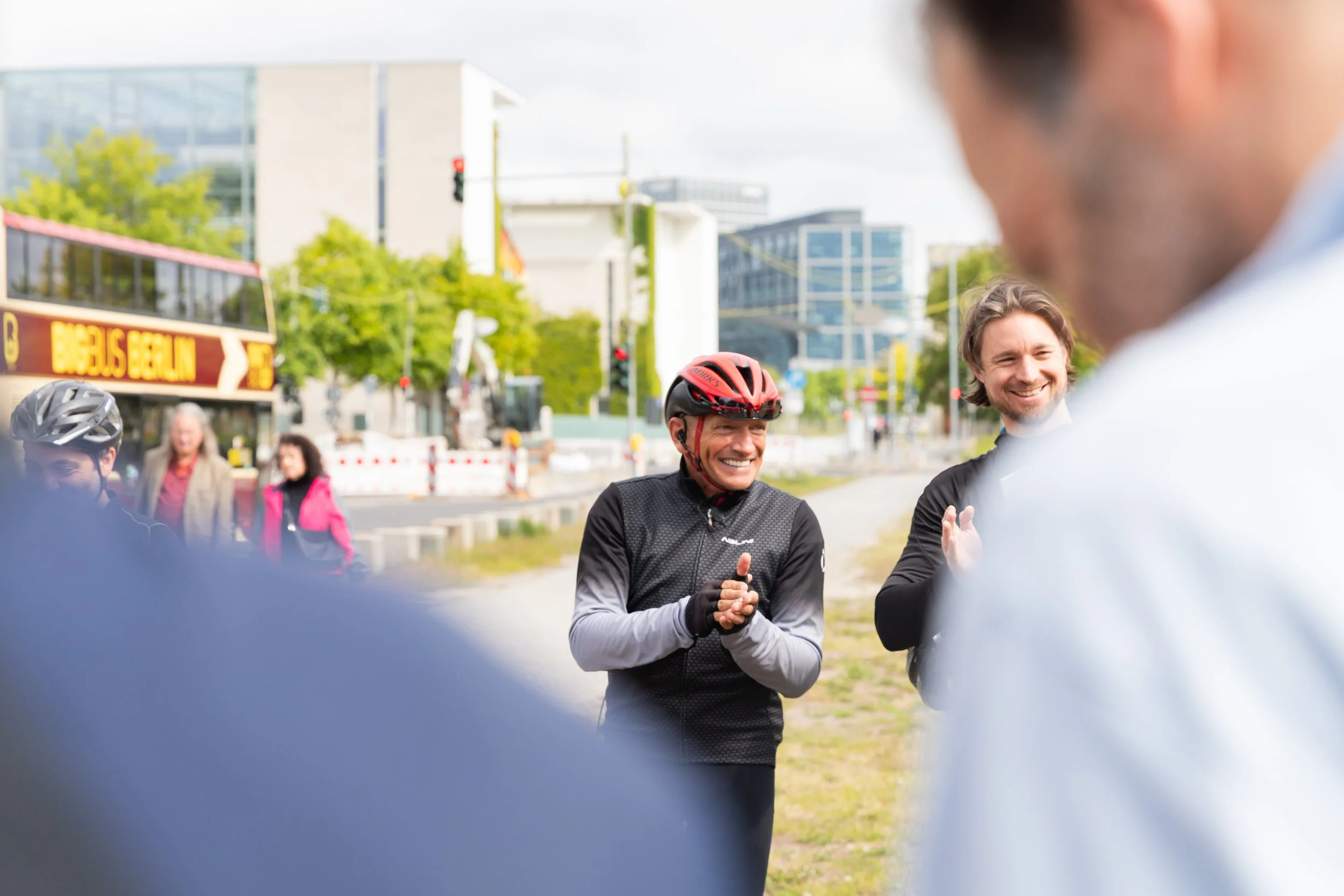 Mehrere Menschen, darunter ein Mann im Fahrradhelm, die draußen lächeln und miteinander sprechen.