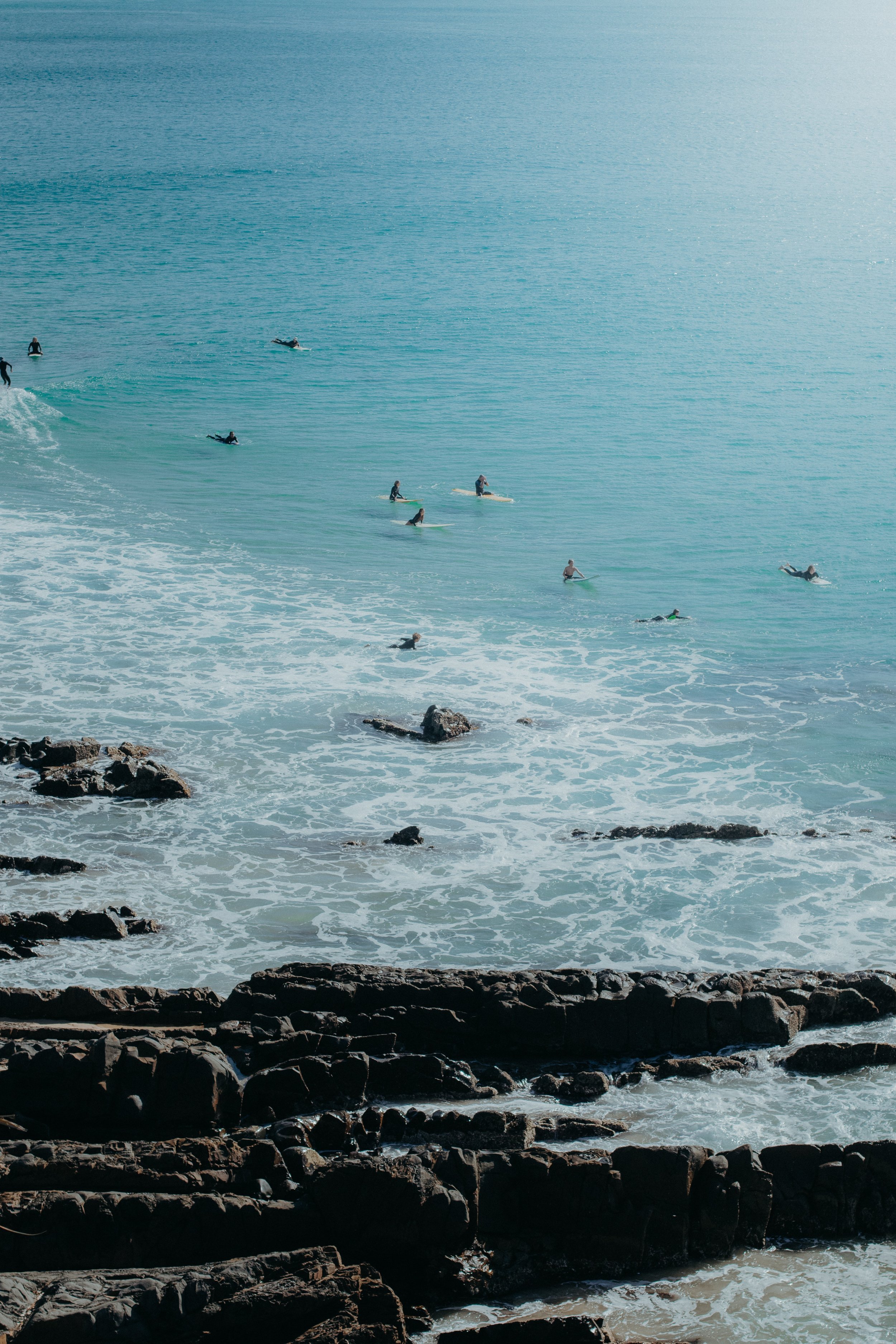 A group of people surfing in the ocean near a rocky shoreline.