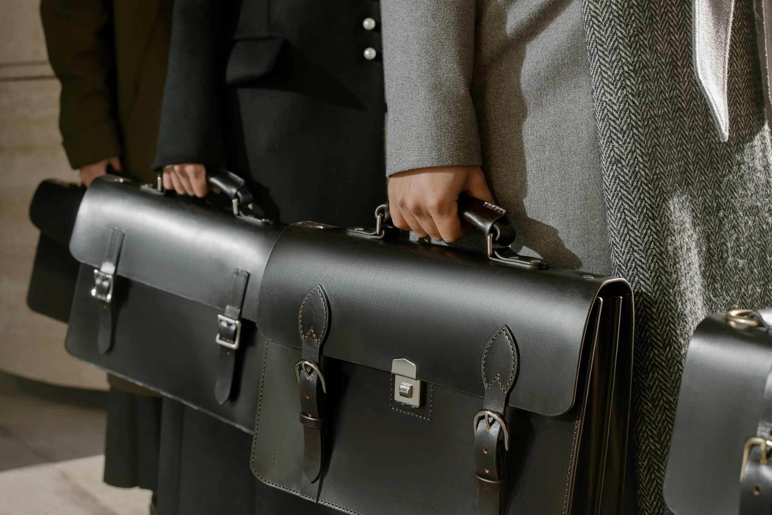 Three people in business attire holding black leather briefcases, standing close together in a professional setting.