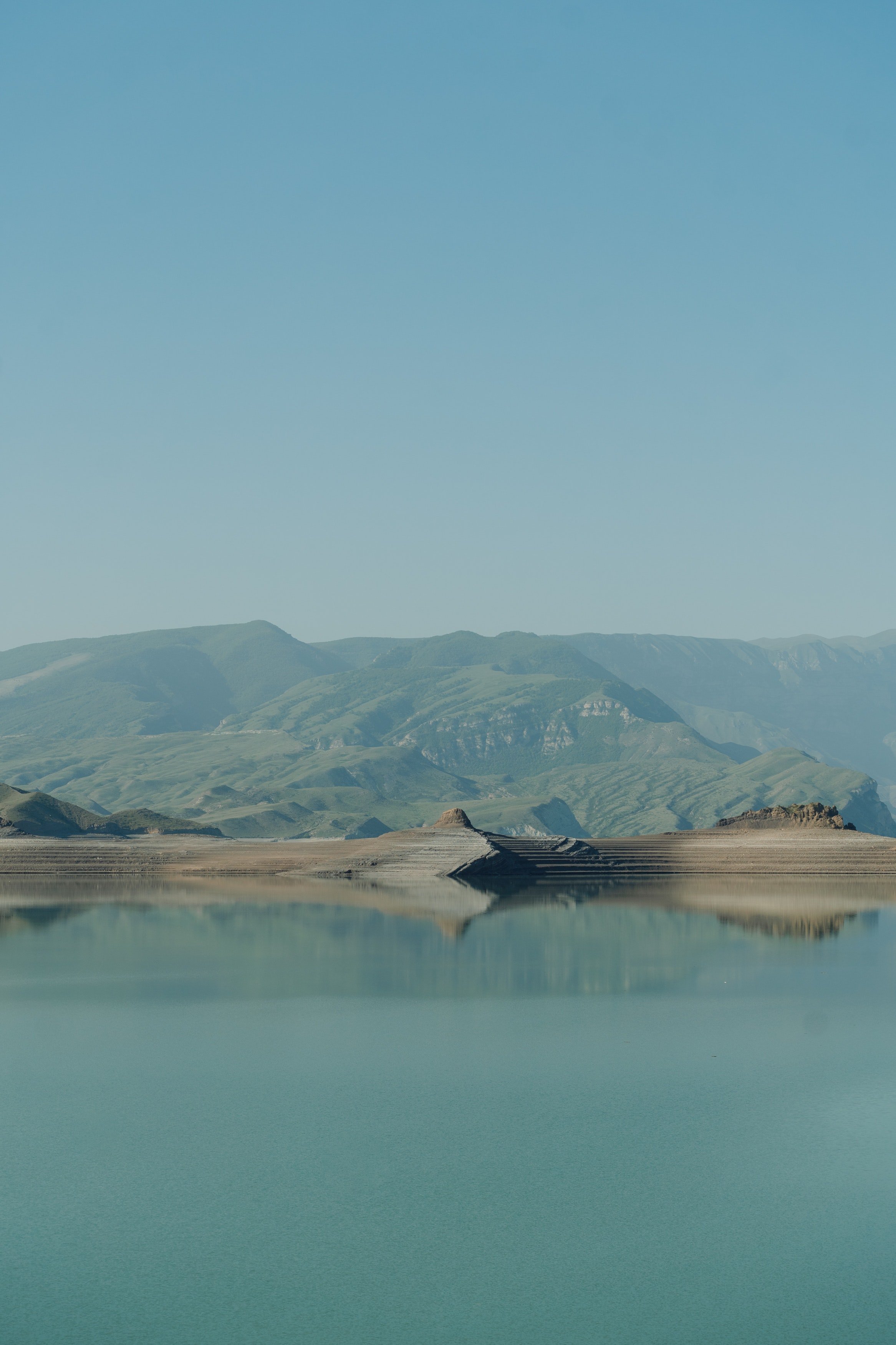 A calm lake with a mountain range in the background under a clear blue sky.
