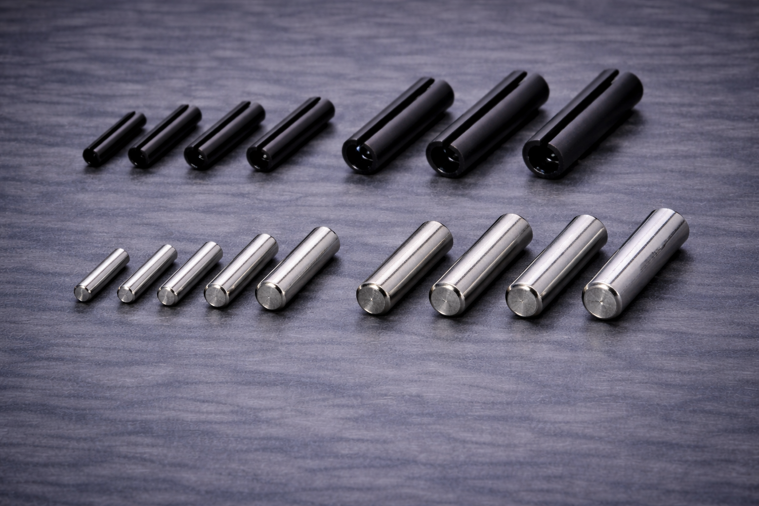 Two rows of metal cylindrical rods, black ones at the top row and silver ones at the bottom row, arranged in increasing size from left to right on a textured dark gray surface.