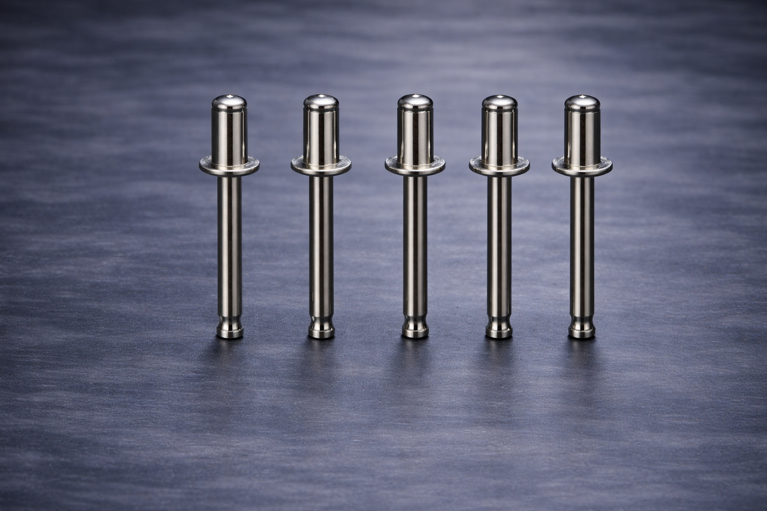 Five metal pins with cylindrical heads standing upright on a dark blue surface.