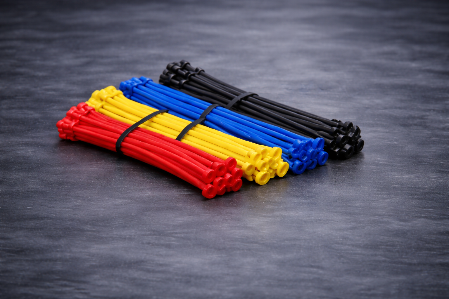 Bundles of colorful rubber bands in red, yellow, blue, and black, organized on a dark surface.