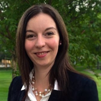 Brianna Brownell with shoulder-length brown hair smiling outdoors with green trees in the background.
